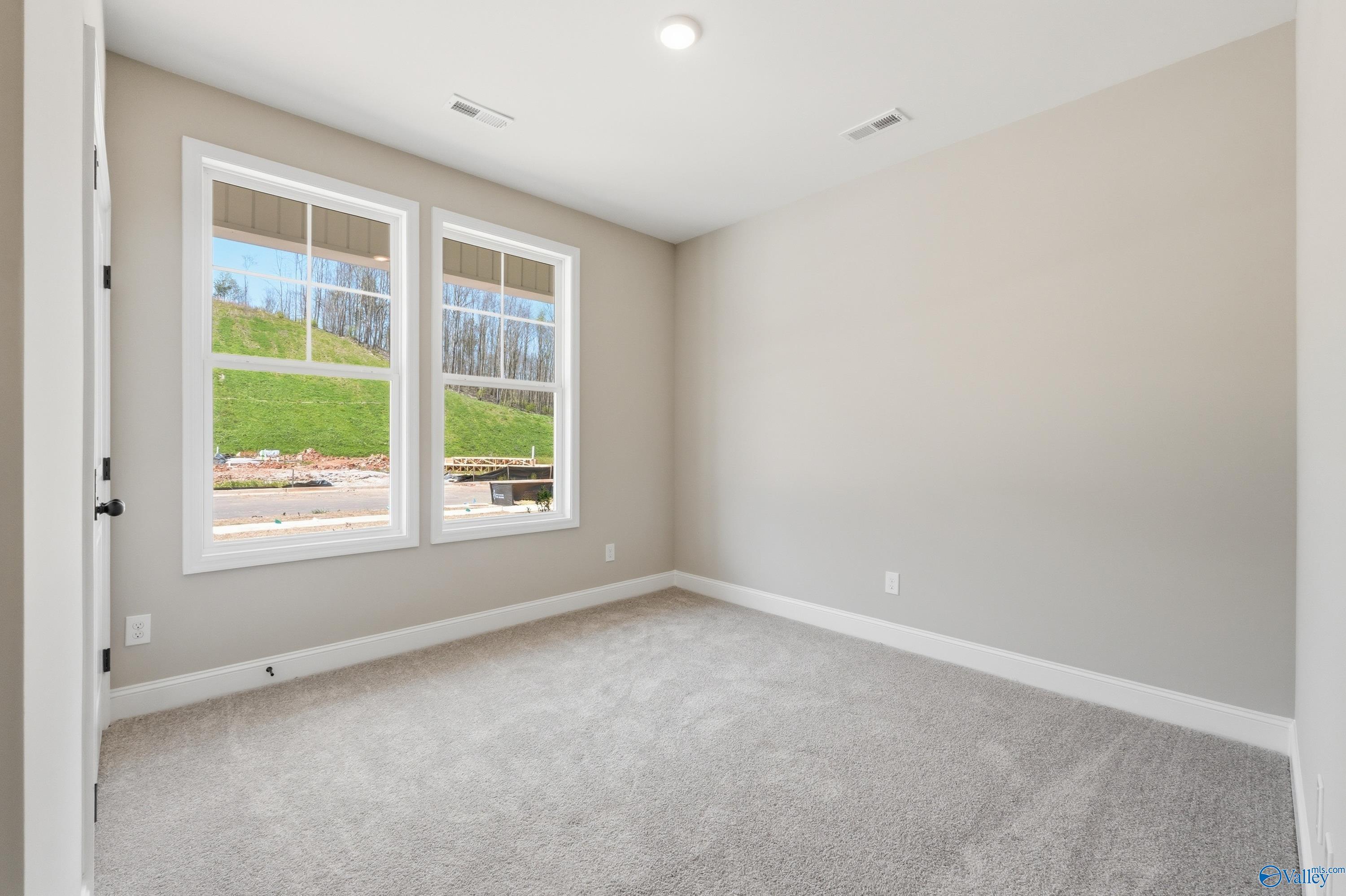 Sunny bedroom with large windows overlooking wooded hill, neutral walls, carpet floor in Davidson Homes The Laurel K, Cullman, AL