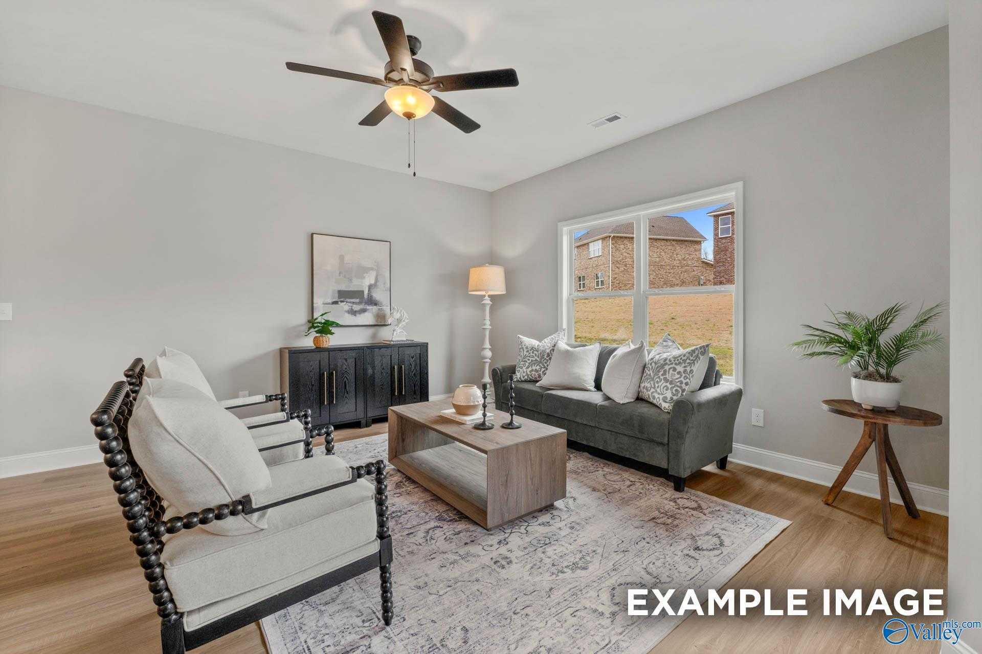 Cozy living room with gray sofa, armchairs, wooden coffee table, ceiling fan and large window view in Davidson Homes The Daphne C, Owens Cross Roads