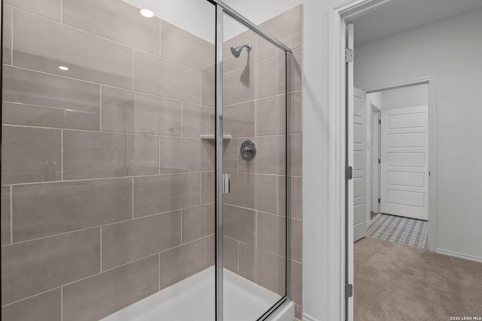Modern walk-in glass shower with neutral tile surround in The Brazos B floor plan by Davidson Homes in Agave, San Antonio.