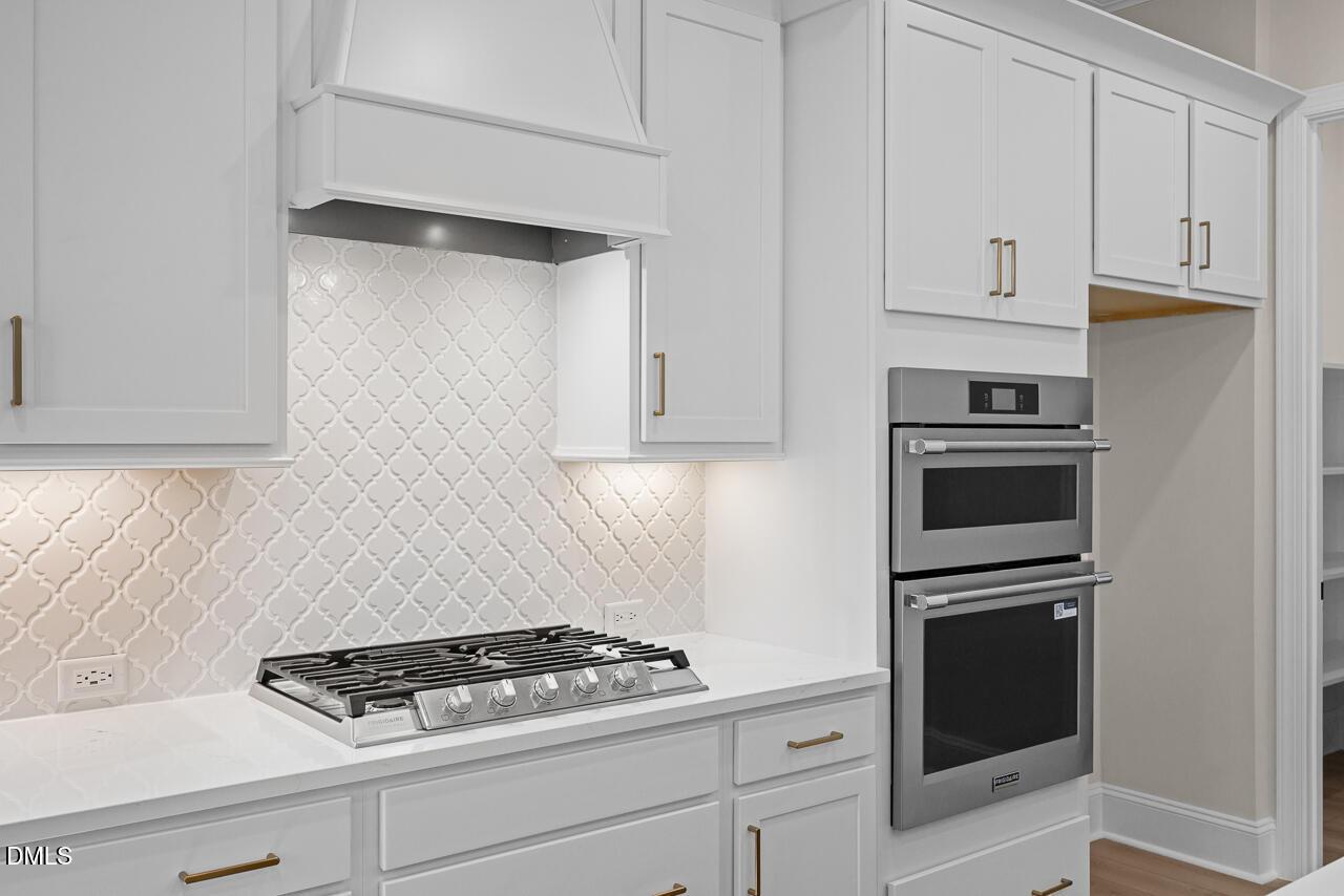 White shaker kitchen with gas cooktop, patterned tile backsplash, and built-in double wall ovens in Davidson Homes Crawford D, Wake Forest NC