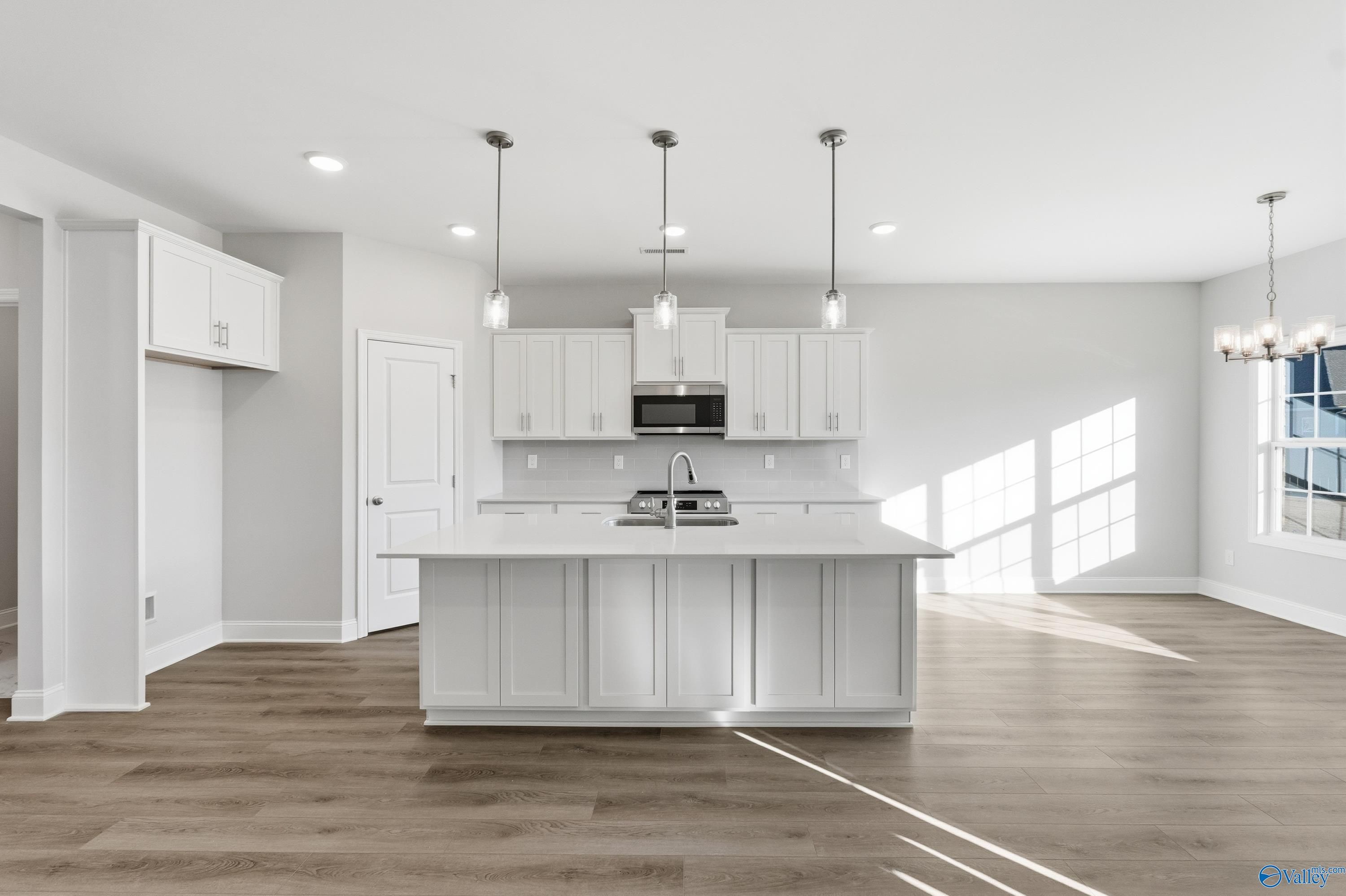 Modern white kitchen with large island sink, stainless appliances, pendant lights in Davidson Homes Montgomery B, Toney, Alabama