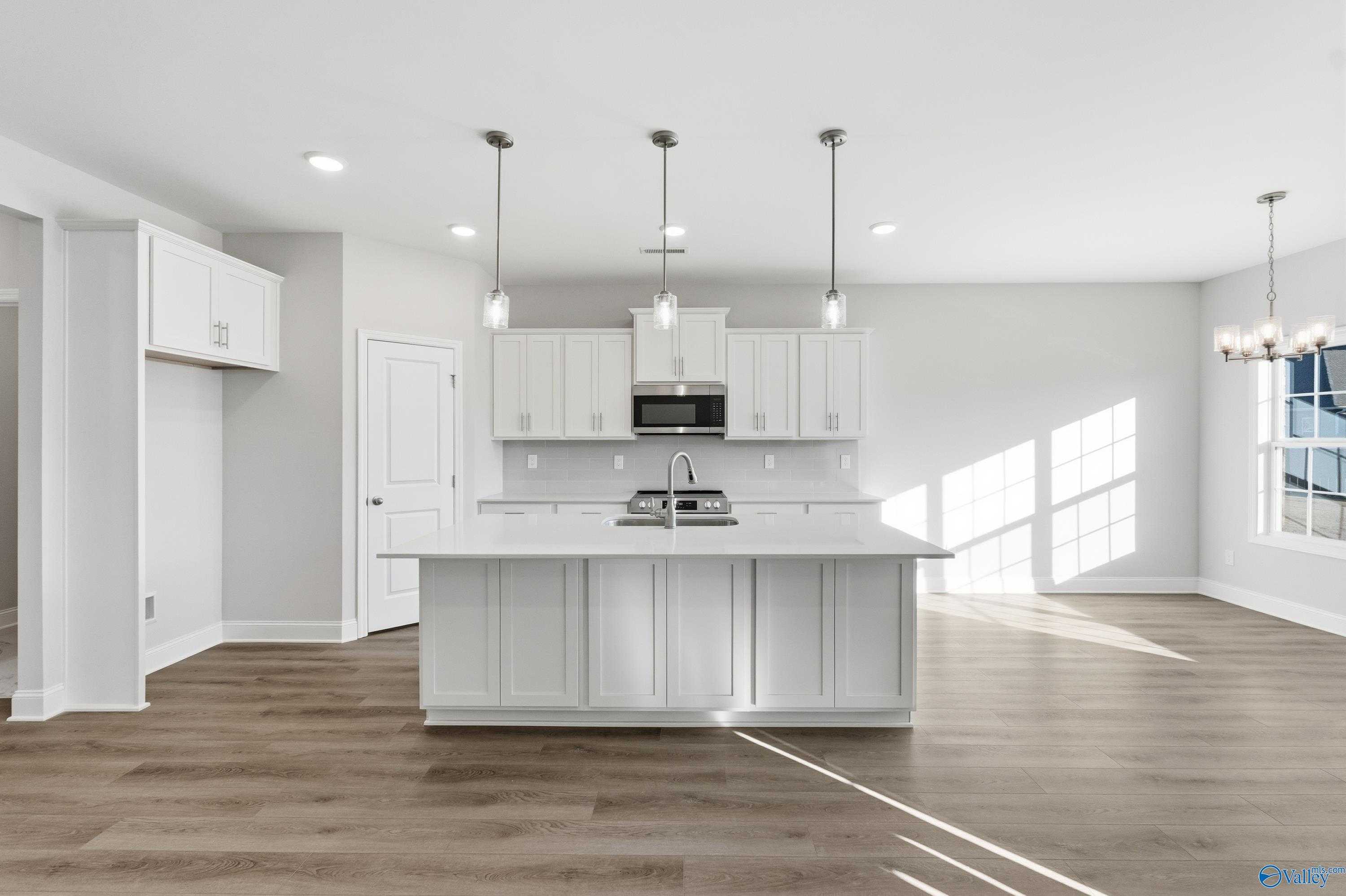Modern white kitchen with large island sink, stainless appliances, pendant lights in Davidson Homes Montgomery B, Toney, Alabama