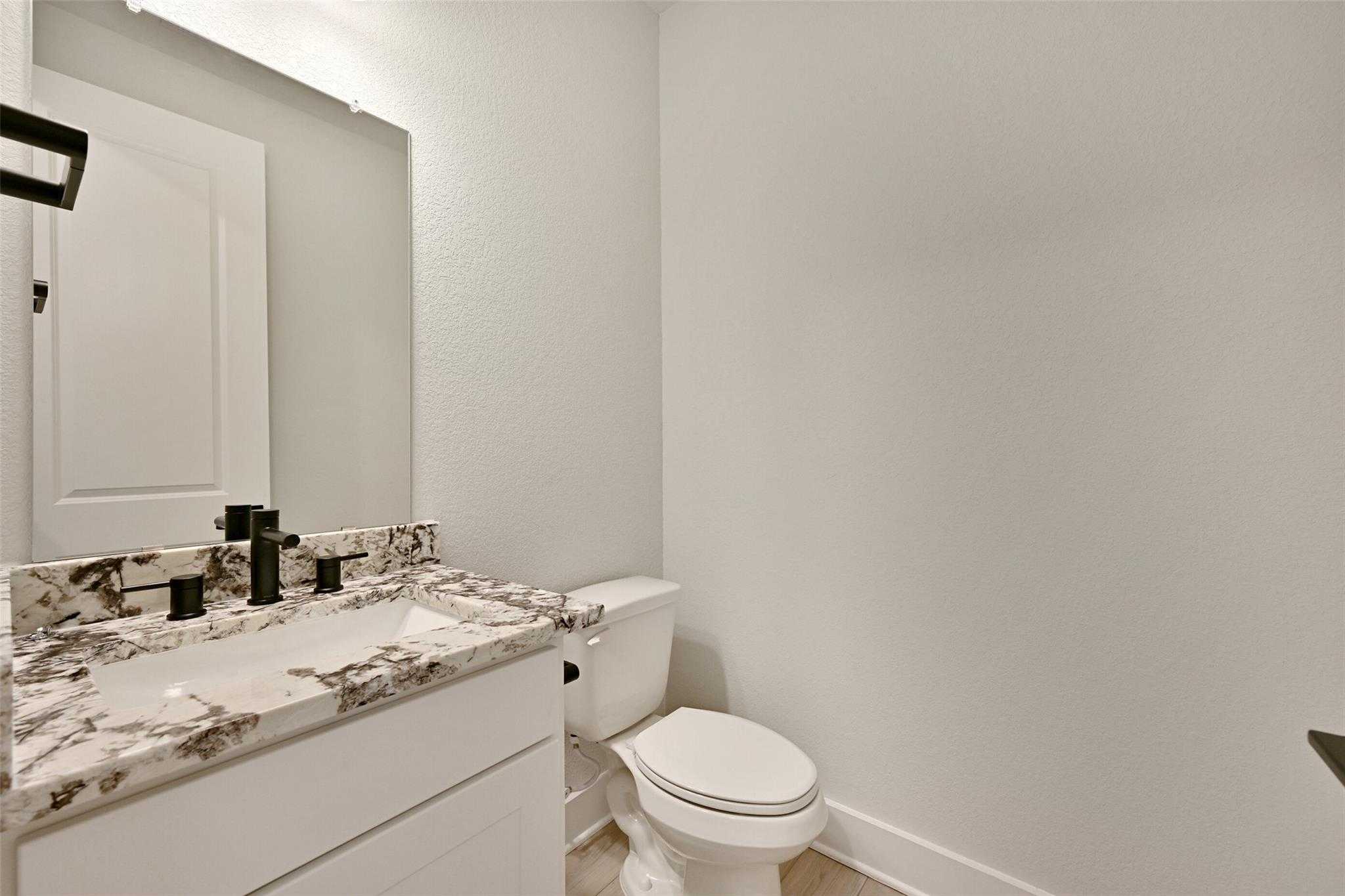 Modern powder room with quartz countertop, black faucet, white vanity and toilet in Davidson Homes The Edward C, Lago Mar, Texas City