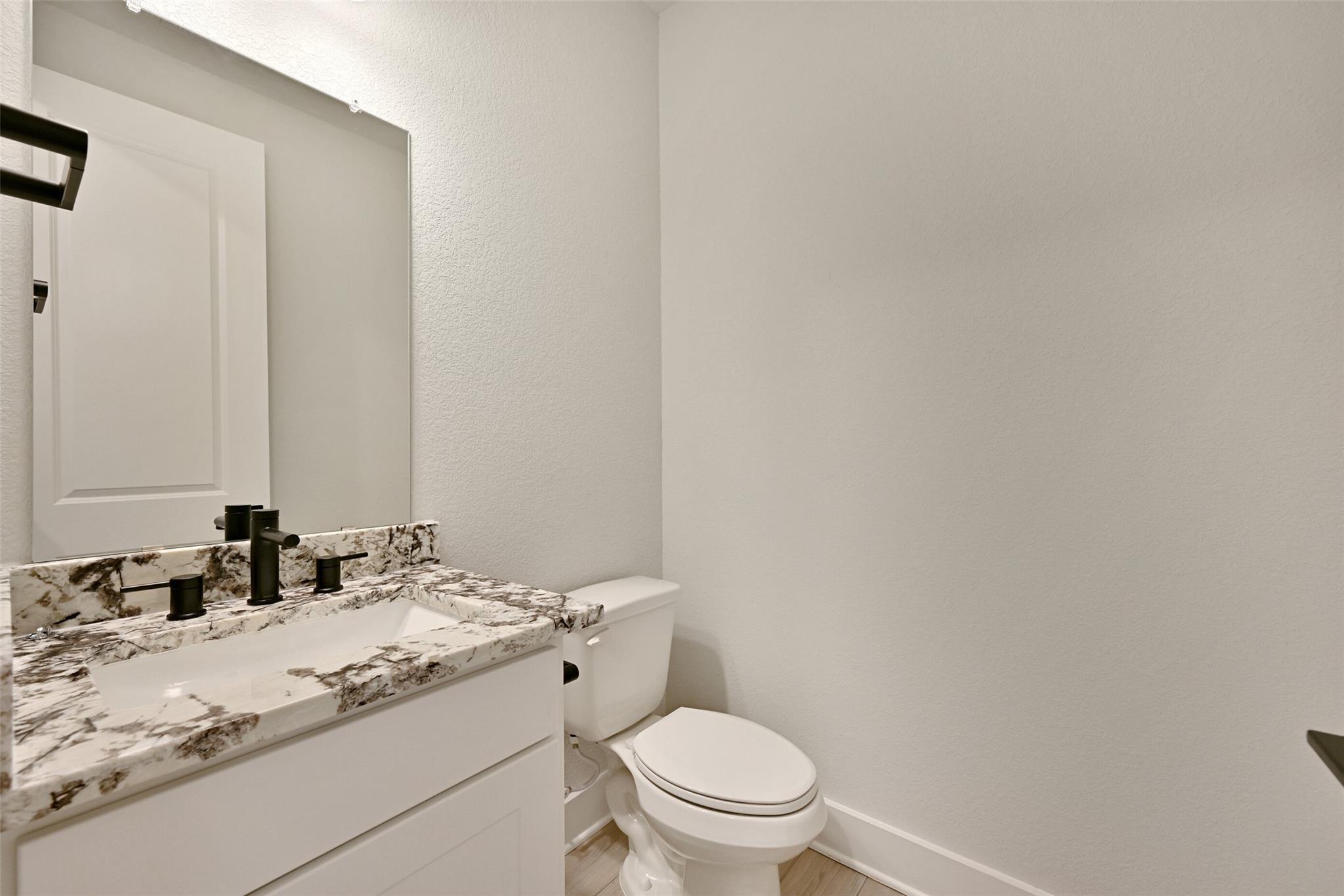 Modern powder room with quartz countertop, black faucet, white vanity and toilet in Davidson Homes The Edward C, Lago Mar, Texas City