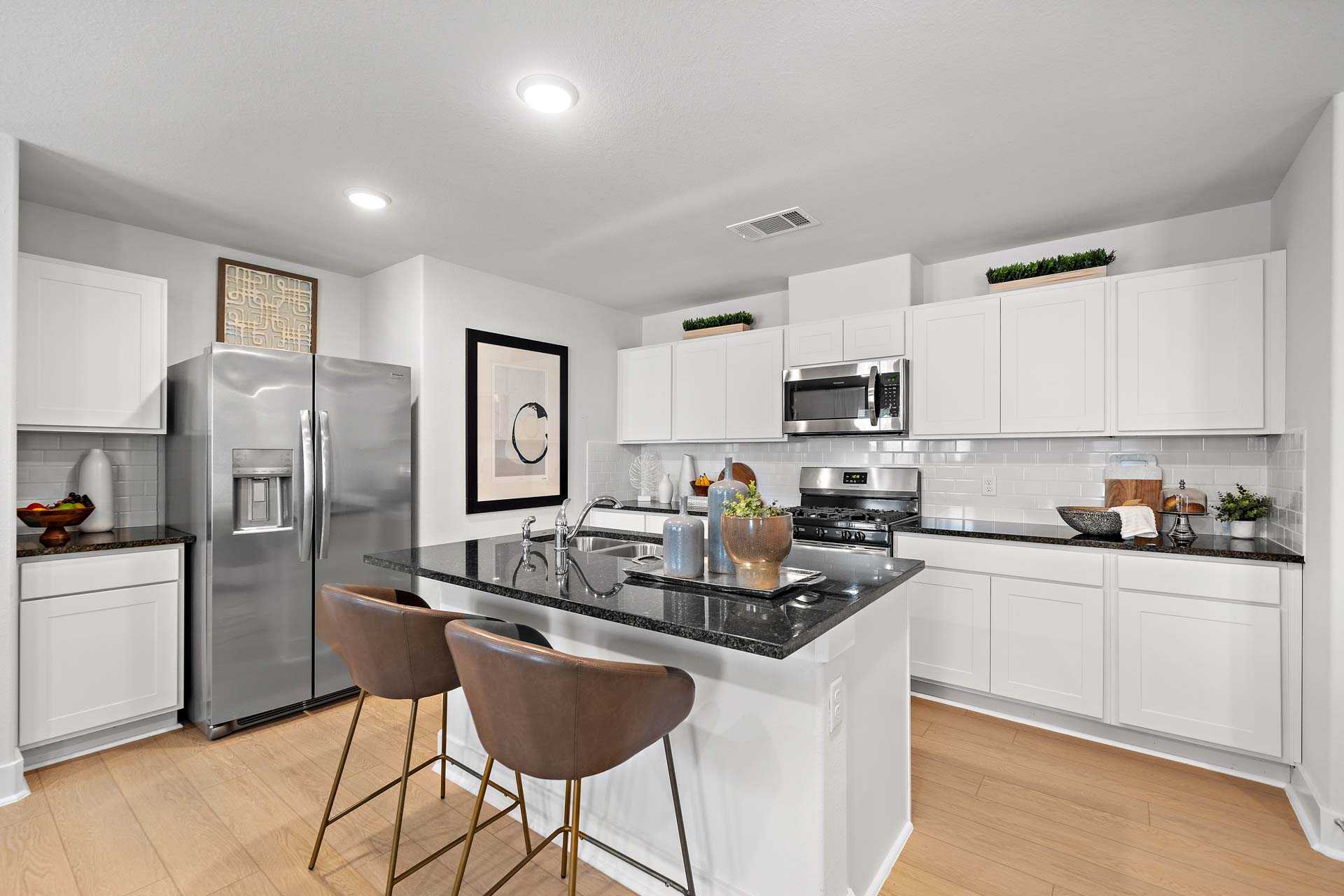 Spacious white kitchen with granite island, stainless appliances, and bar stools at Haven at Kieth Harrow, Cypress TX