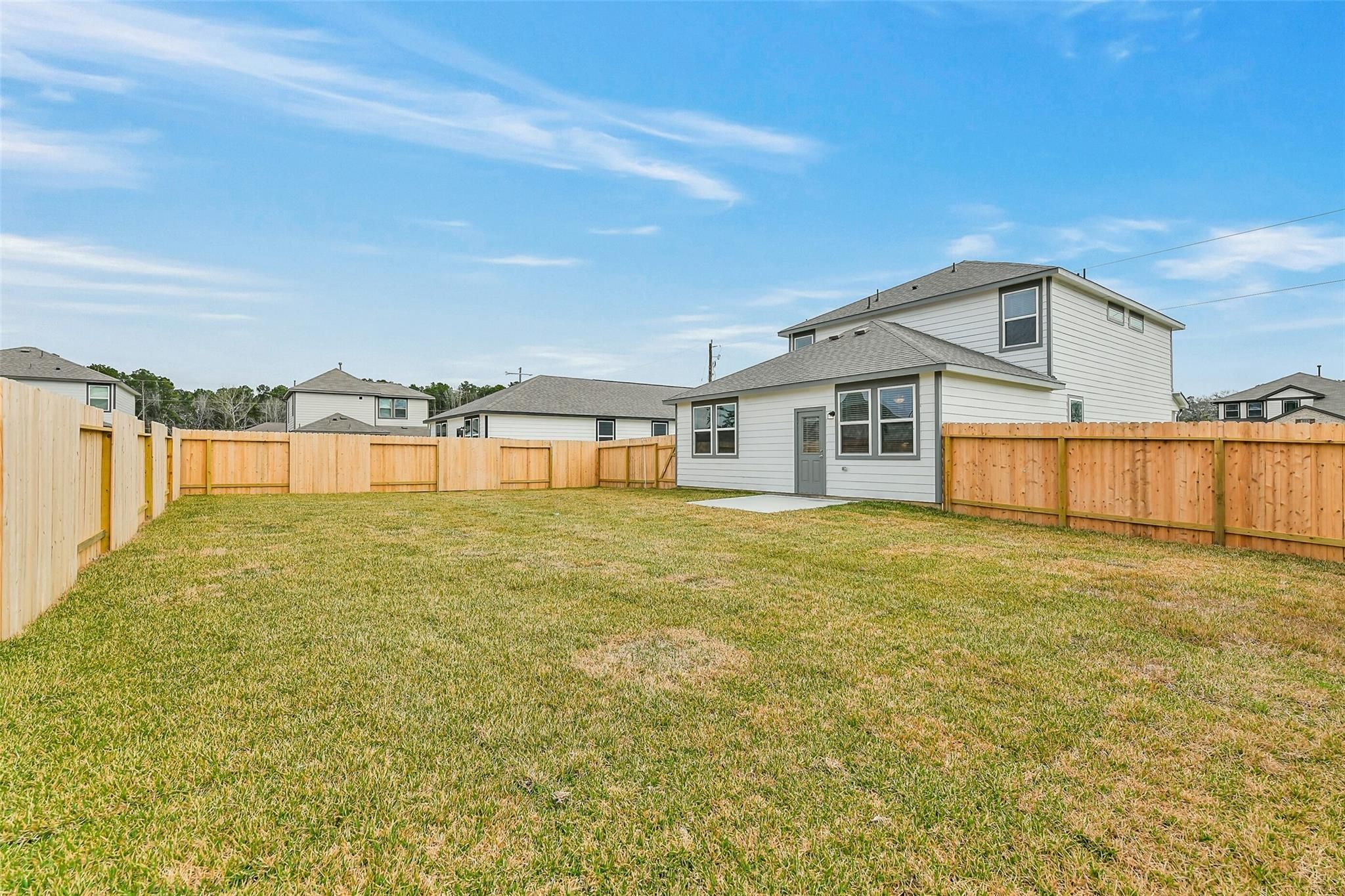 Fenced backyard with lush green lawn and two-story white home, 2-car garage, in Davidson Homes The Brazos E, Liberty Estates, Cleveland, Texas