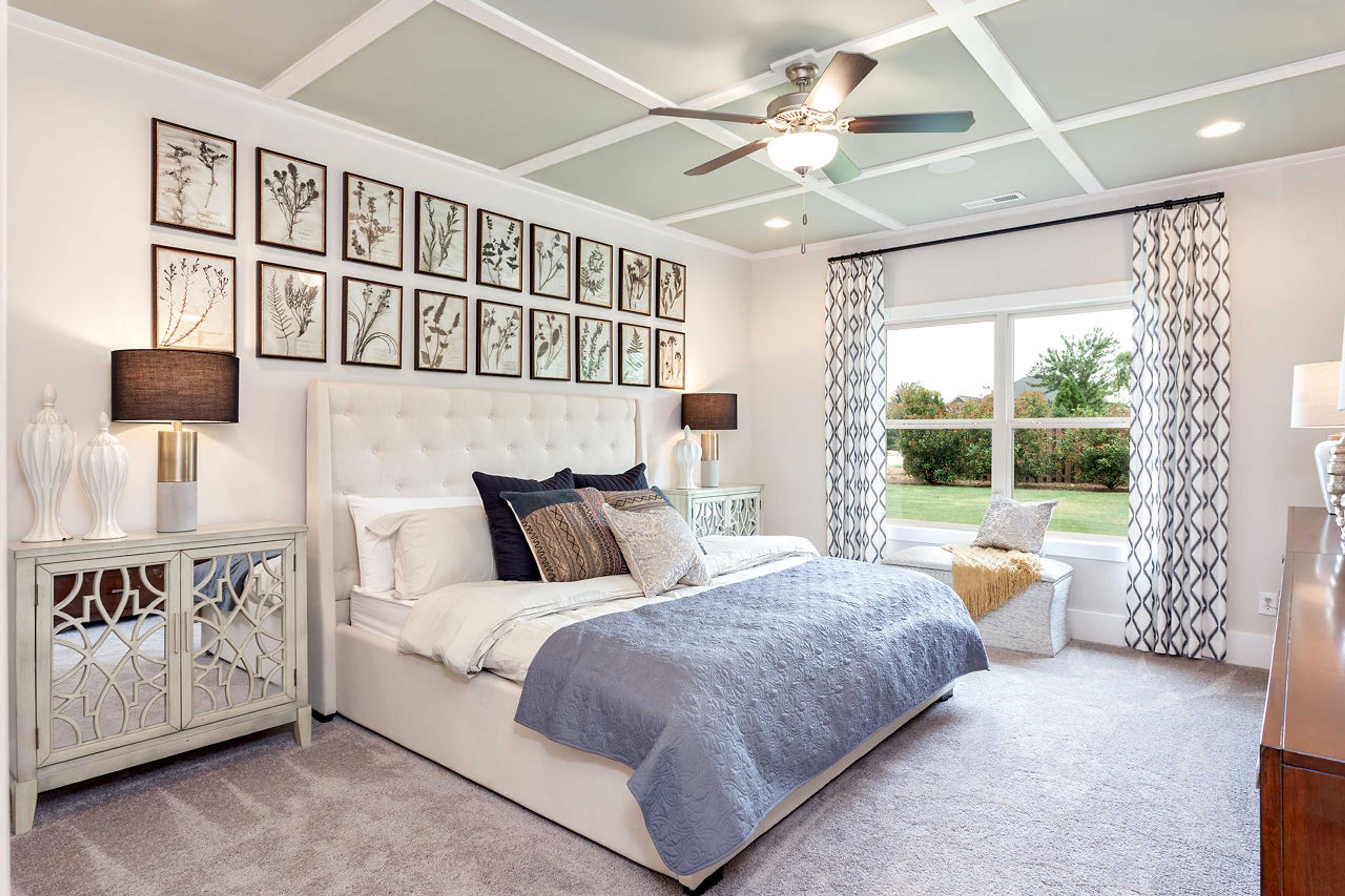 Spacious master bedroom at Williams Pointe in Huntsville AL with green beamed ceiling, king bed, botanical wall art, and garden view