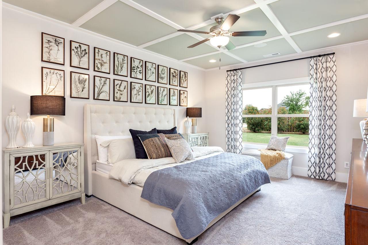 Spacious master bedroom at Williams Pointe in Huntsville AL with green beamed ceiling, king bed, botanical wall art, and garden view