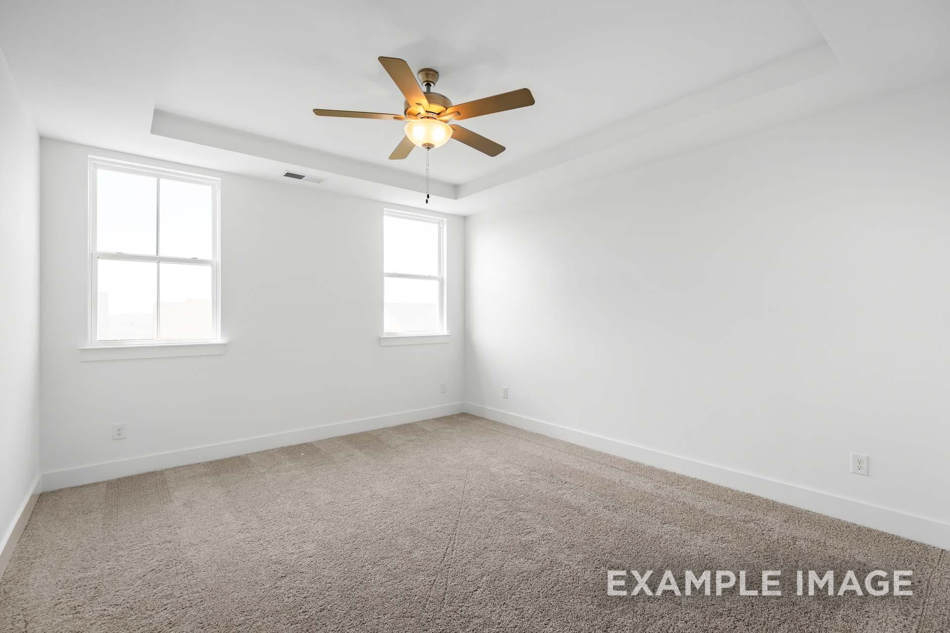 Bright secondary bedroom in The Ash C design featuring white walls, beige carpet, dual windows, and ceiling fan