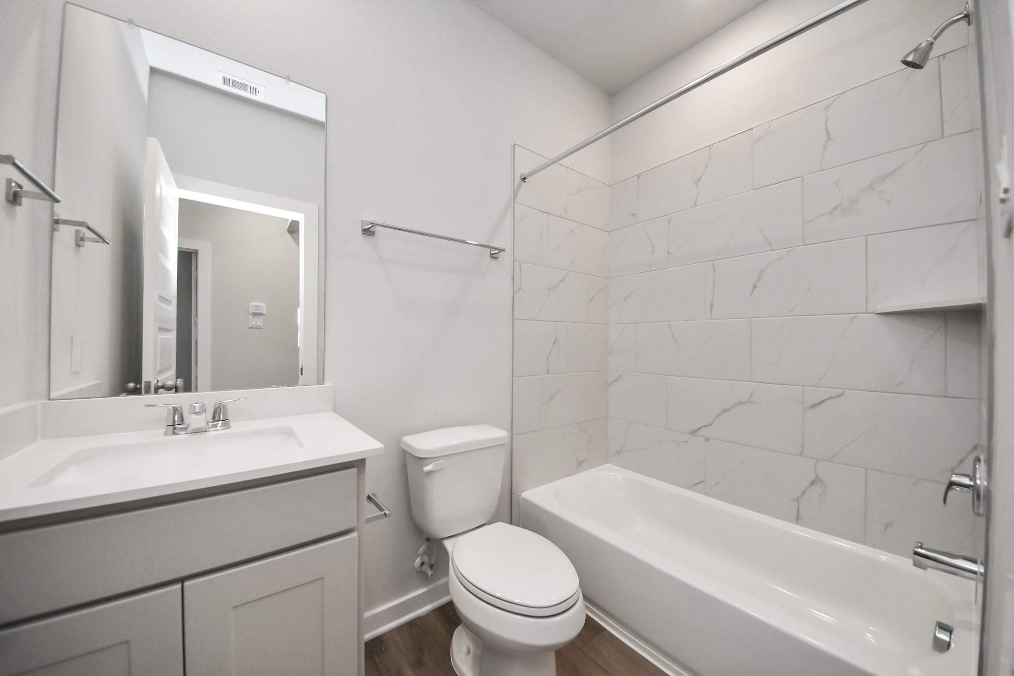 Modern bathroom with marble tile tub surround, vanity sink, and toilet in Davidson Homes The Frio F plan, Robins Landing Houston