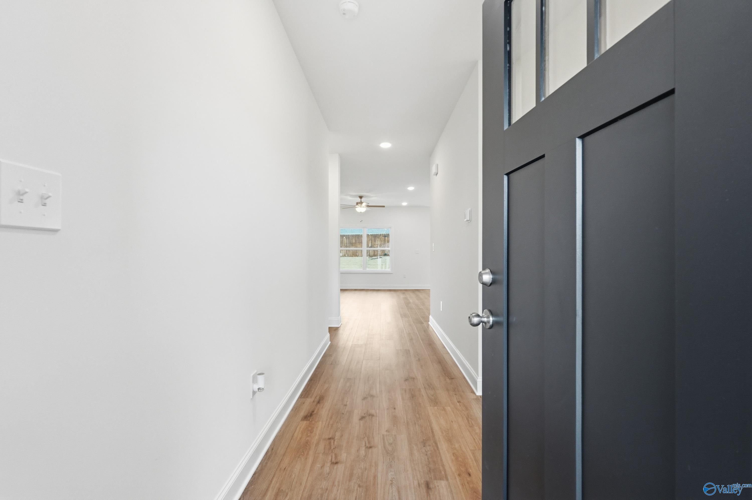 Bright hallway with light oak floors, white walls, and recessed lights leading to black front door in Davidson Homes The Asheville C, Meridianville