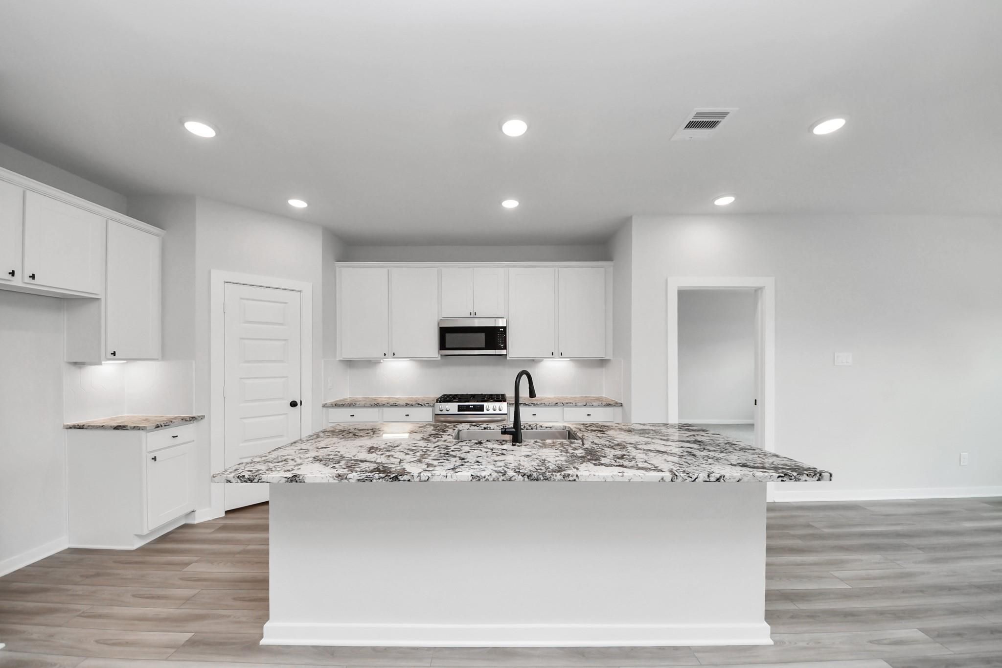 Modern kitchen with white cabinets, granite island, and stainless appliances in The Everett C home, River Ranch Meadows.