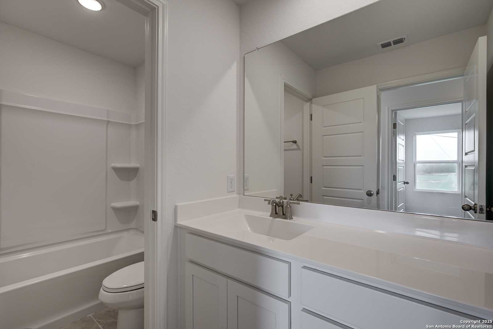 Bright master bathroom with white vanity, large mirror, bathtub-shower combo in Davidson Homes The Trinity A, San Antonio