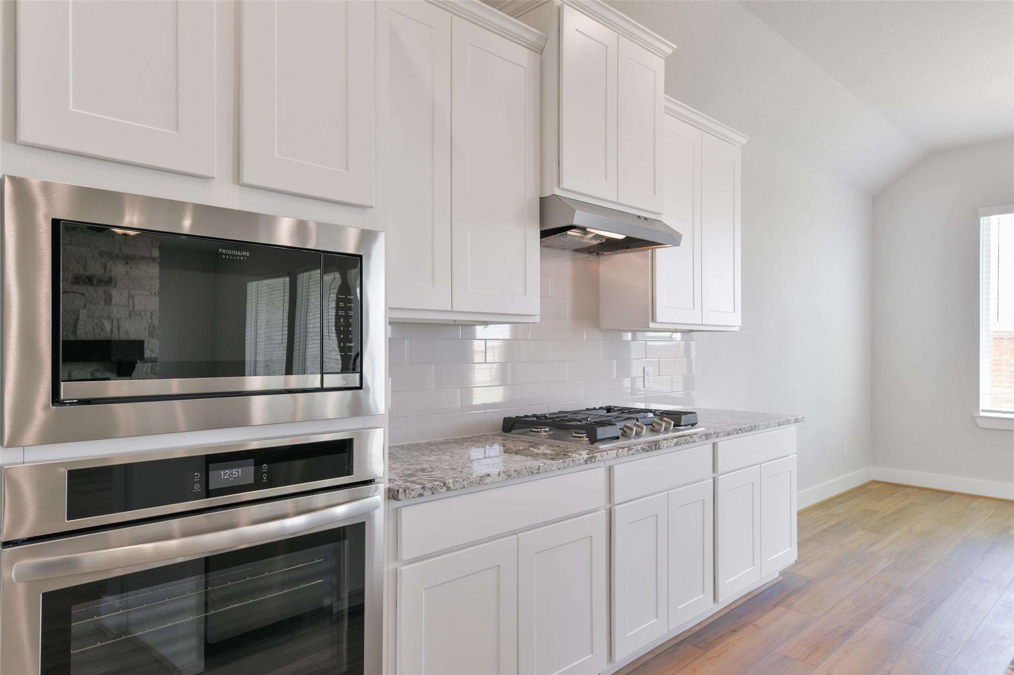 Modern white shaker kitchen with stainless double oven, gas cooktop, granite counters in Davidson Homes The Edward A, Texas City, Texas