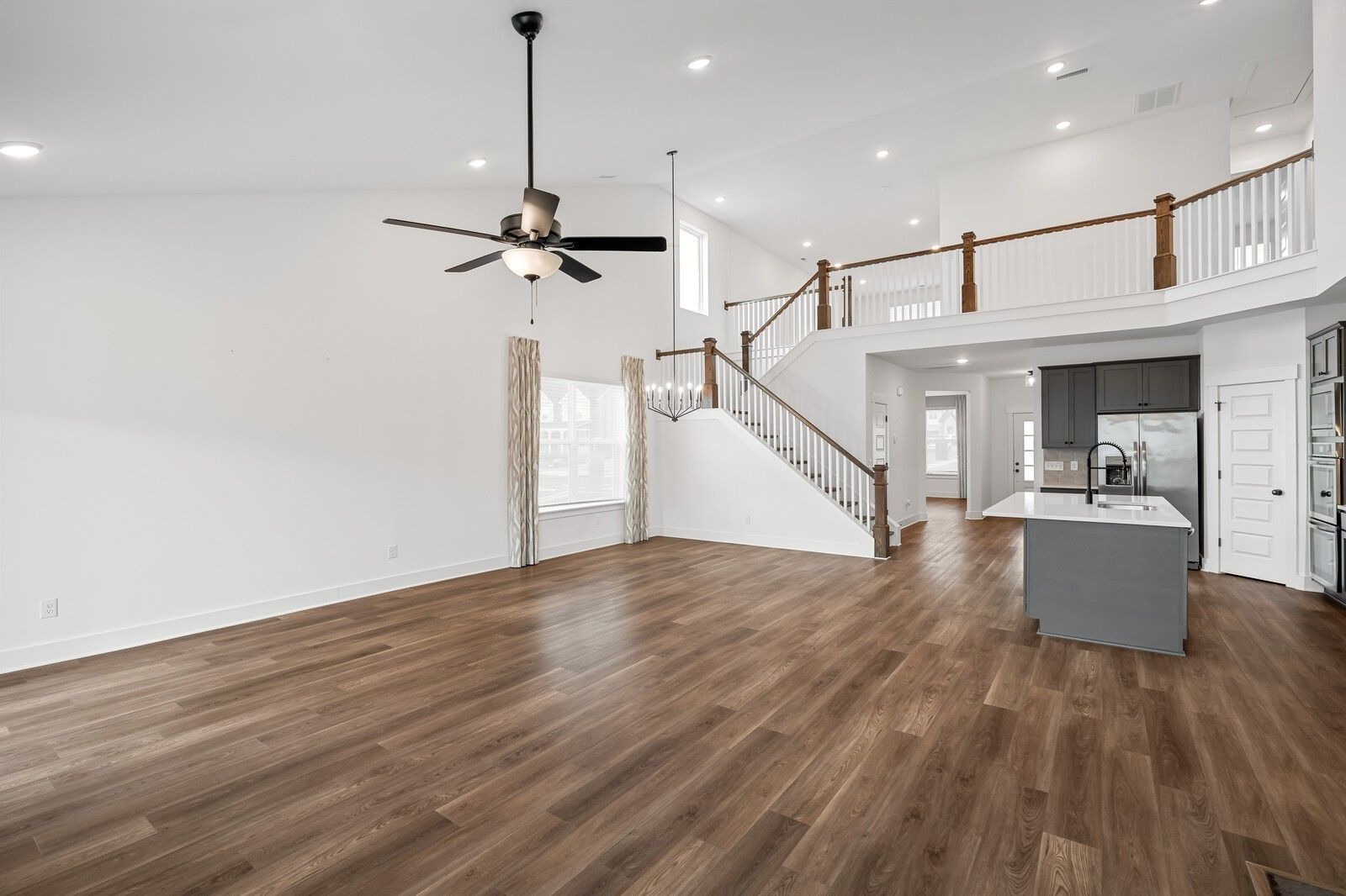 Spacious two-story open living area with hardwood floors, ceiling fan, curved staircase, and modern kitchen island in Davidson Homes Ridgeport, Gallatin TN