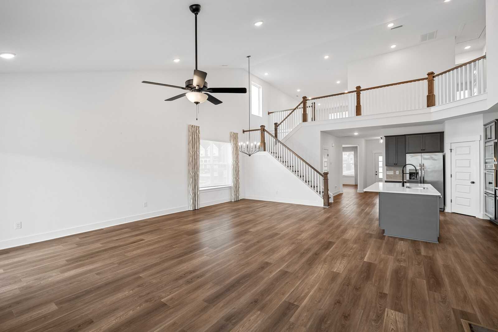 Spacious two-story open living area with hardwood floors, ceiling fan, curved staircase, and modern kitchen island in Davidson Homes Ridgeport, Gallatin TN
