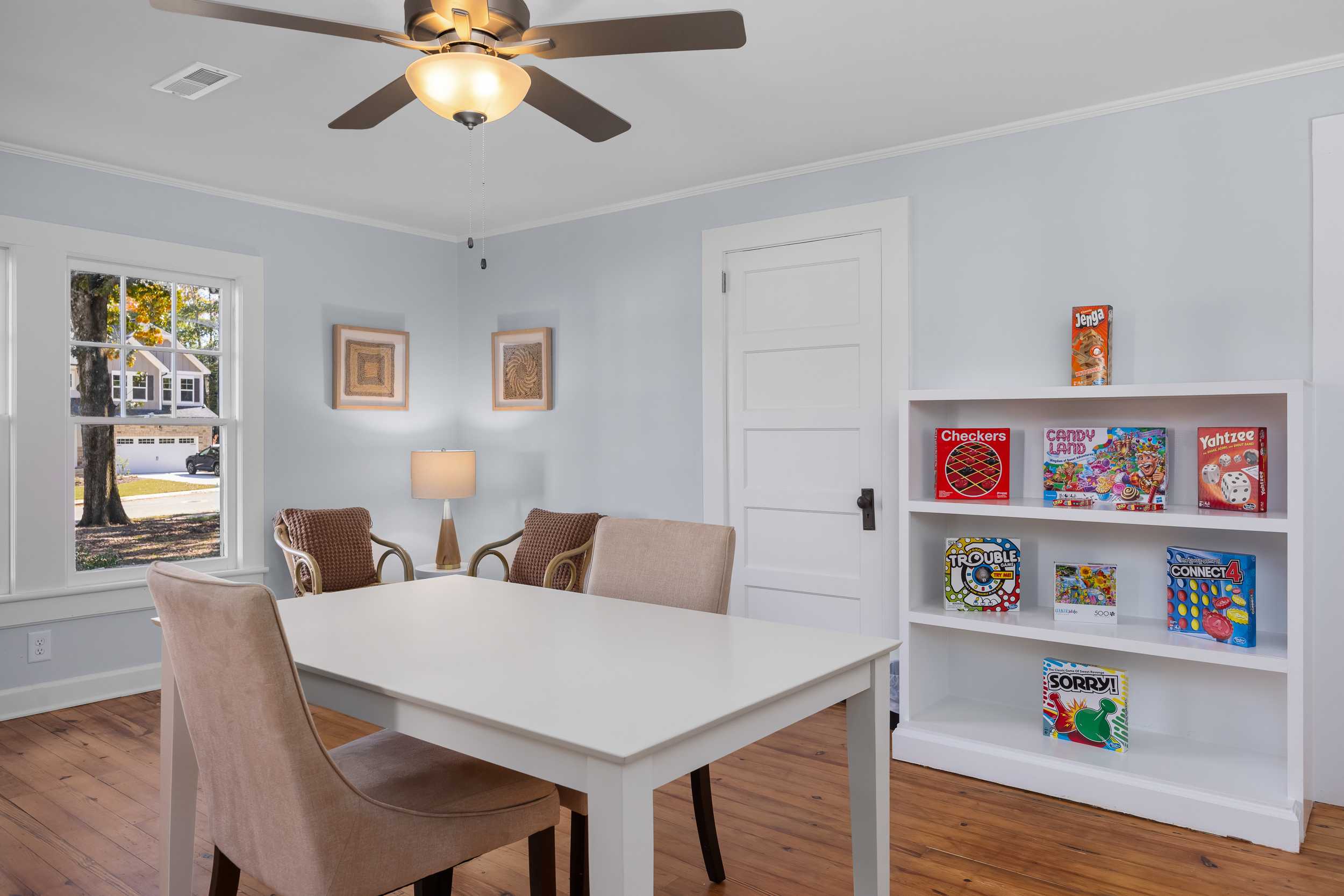 Cozy playroom at Stagecoach Corner in Mebane NC with board games bookshelf, wooden table and chairs, ceiling fan, lamp, hardwood floors
