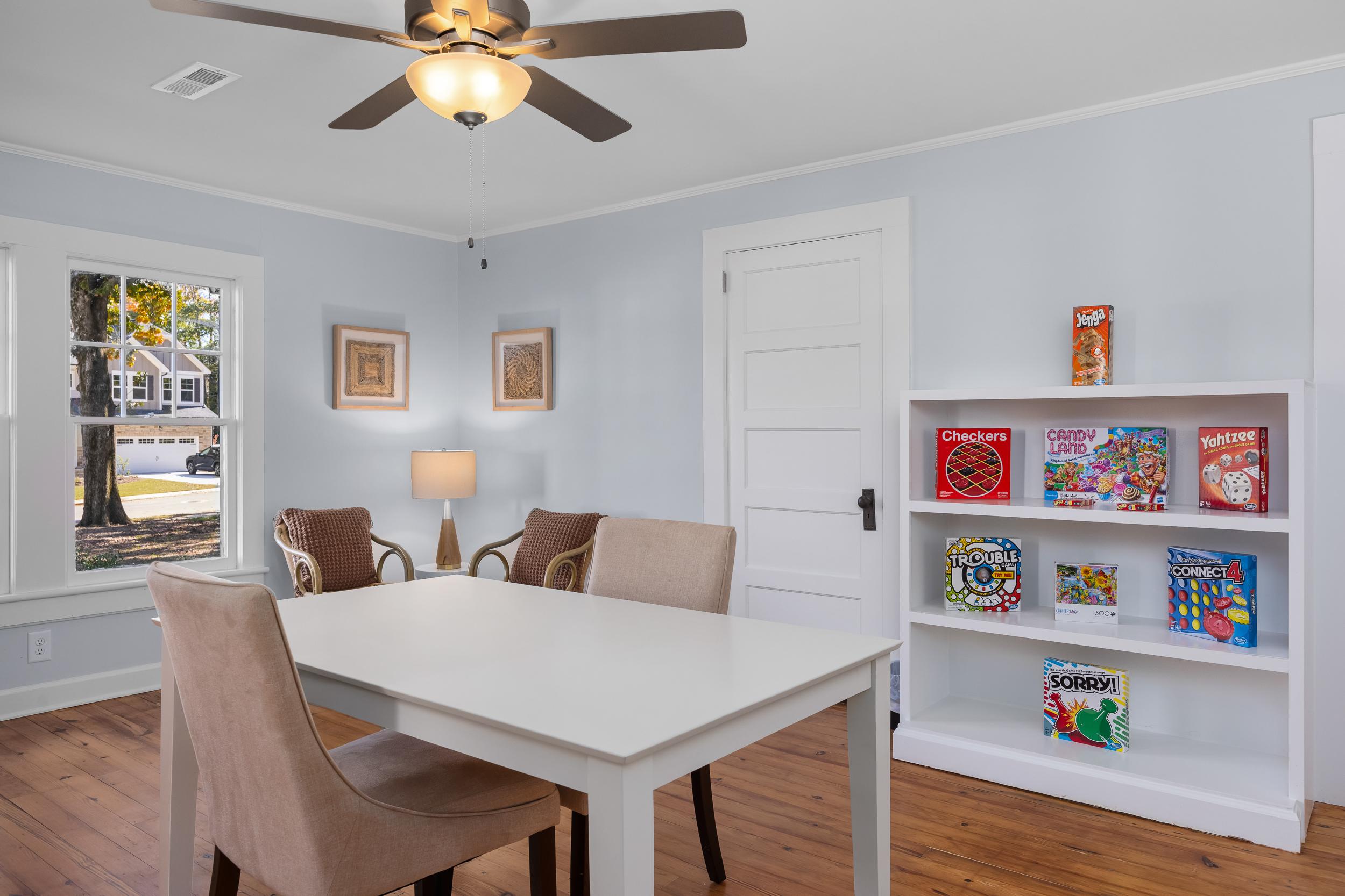 Cozy playroom at Stagecoach Corner in Mebane NC with board games bookshelf, wooden table and chairs, ceiling fan, lamp, hardwood floors