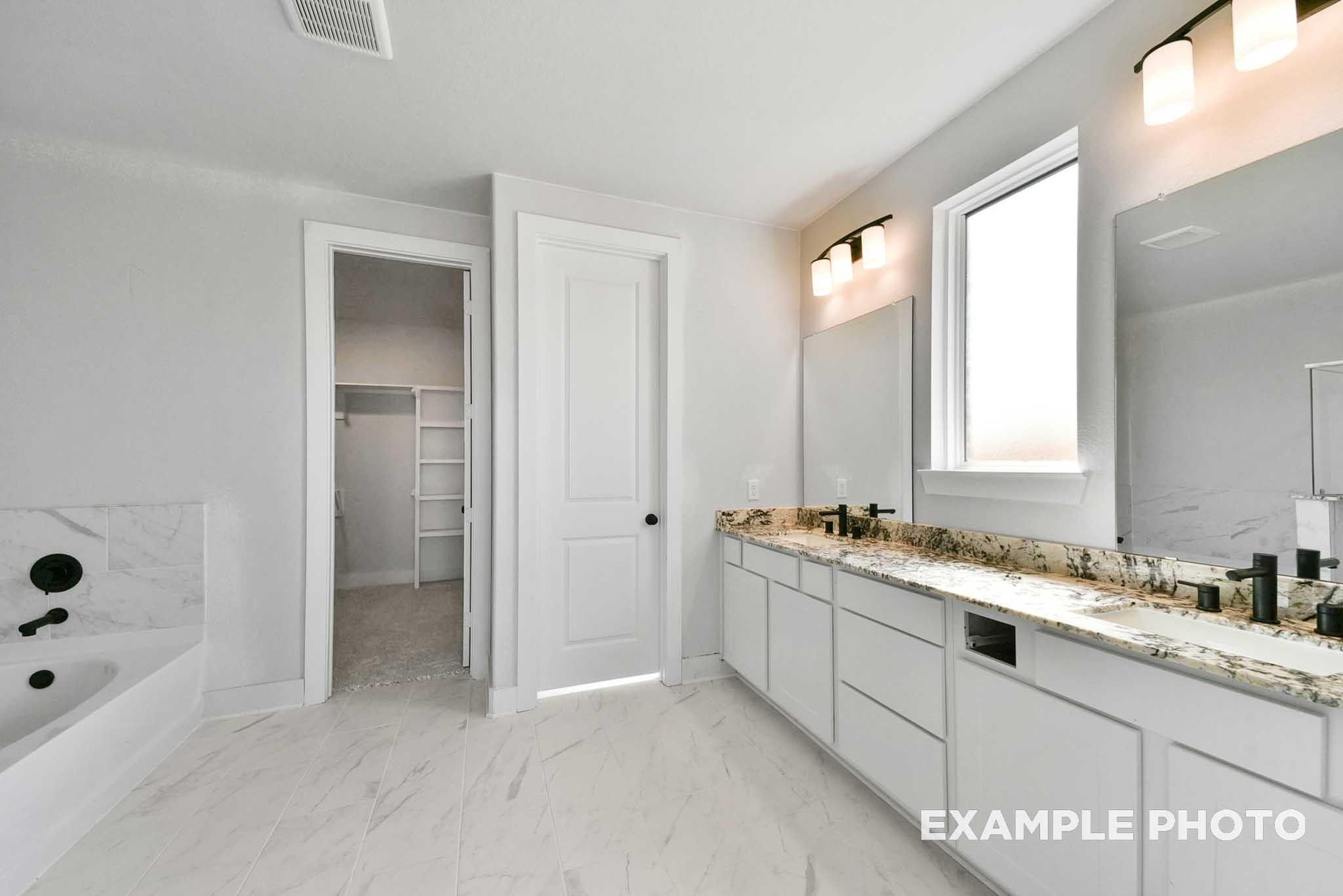 Elegant master bathroom with double vanity, quartz counters, freestanding tub, and walk-in closet in Davidson Homes The George A, Texas City