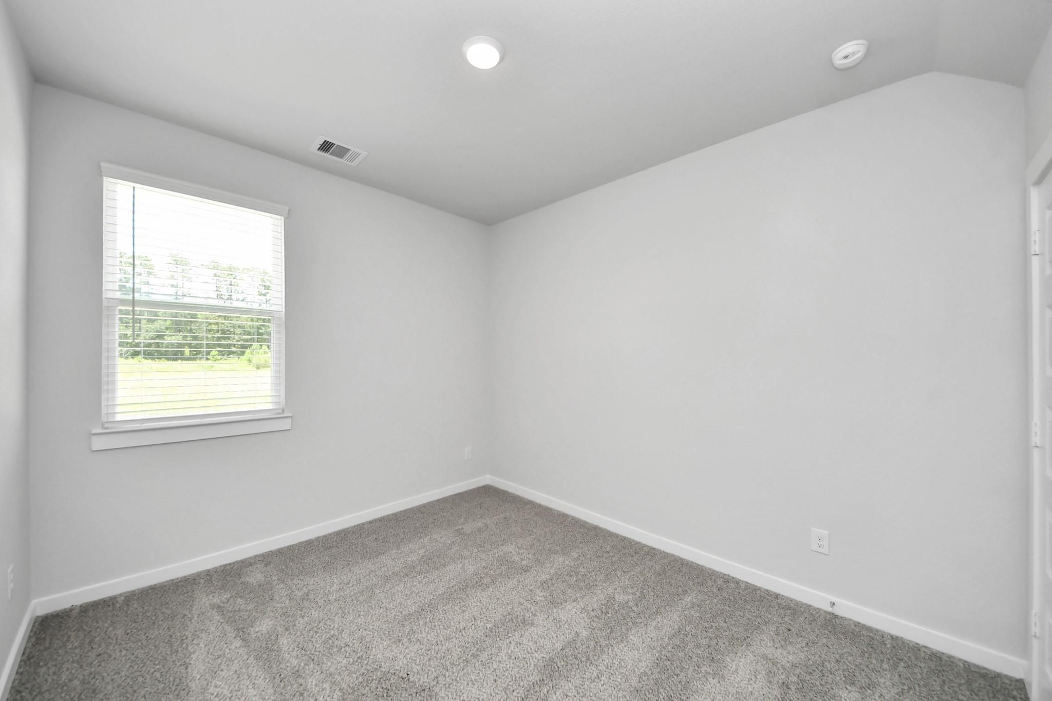 Bright, carpeted bedroom with neutral walls in The Sabine E floor plan at Liberty Estates, Cleveland, Texas.
