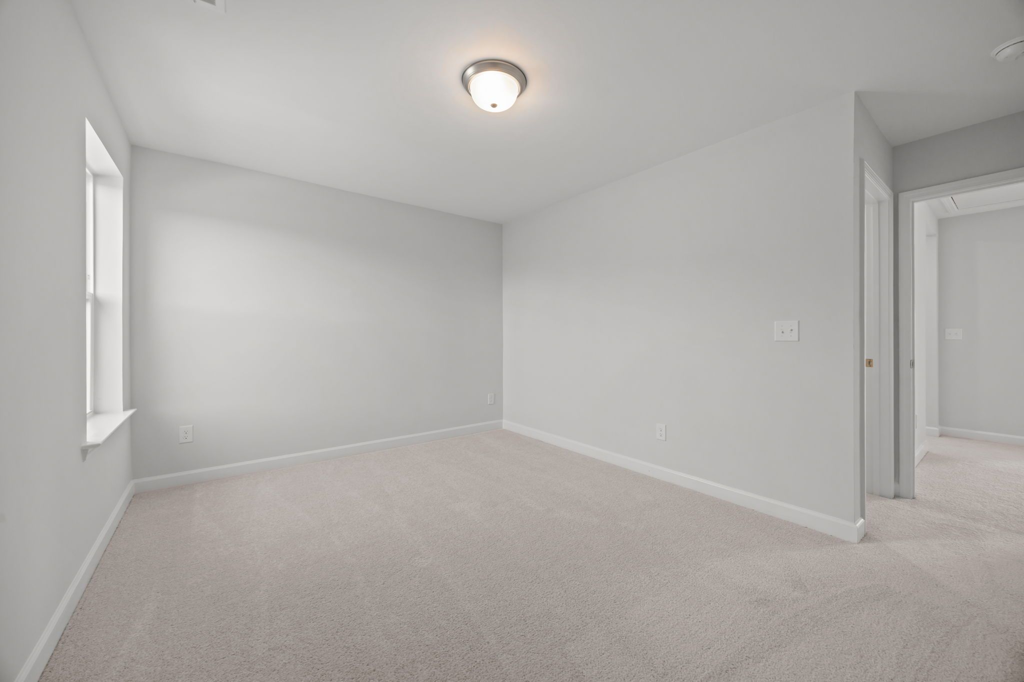 Bright, carpeted bedroom in The Ashport by Davidson Homes featuring neutral walls, natural light, and modern fixtures.