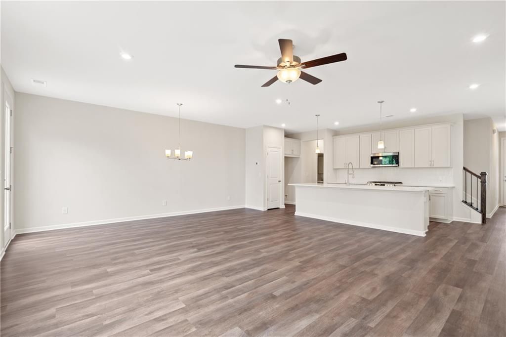 Open-concept living and kitchen with hardwood floors, ceiling fan, white cabinets, and island in The Cary B floor plan, Kennesaw, Georgia