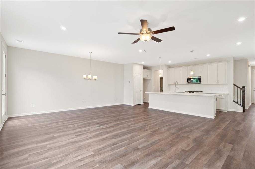 Open-concept living and kitchen with hardwood floors, ceiling fan, white cabinets, and island in The Cary B floor plan, Kennesaw, Georgia