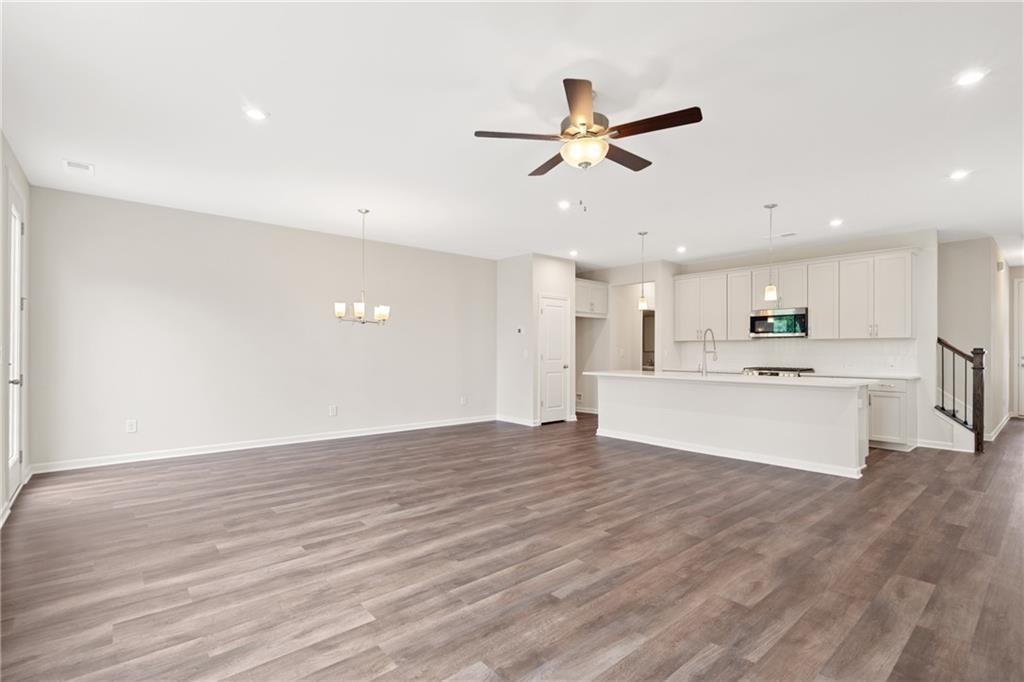 Open-concept living and kitchen with hardwood floors, ceiling fan, white cabinets, and island in The Cary B floor plan, Kennesaw, Georgia