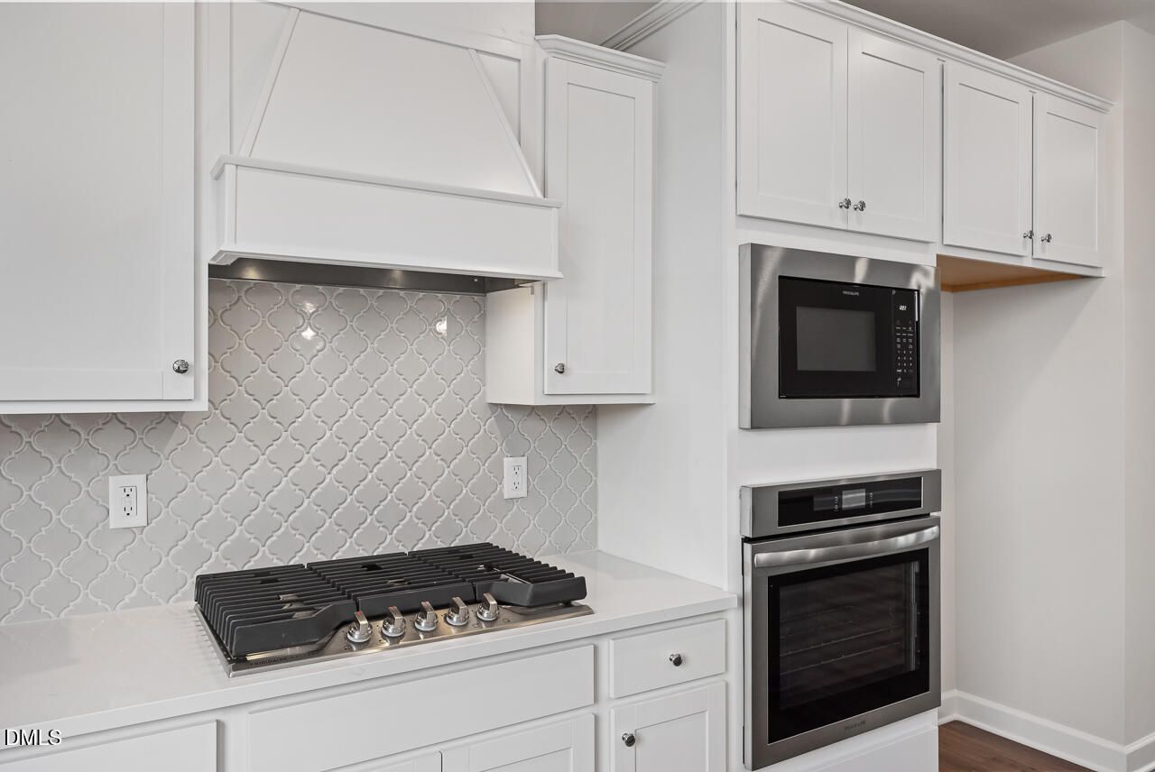 Modern kitchen with white cabinets, tile backsplash, and stainless steel appliances in The Avery Interior, Knightdale, NC.