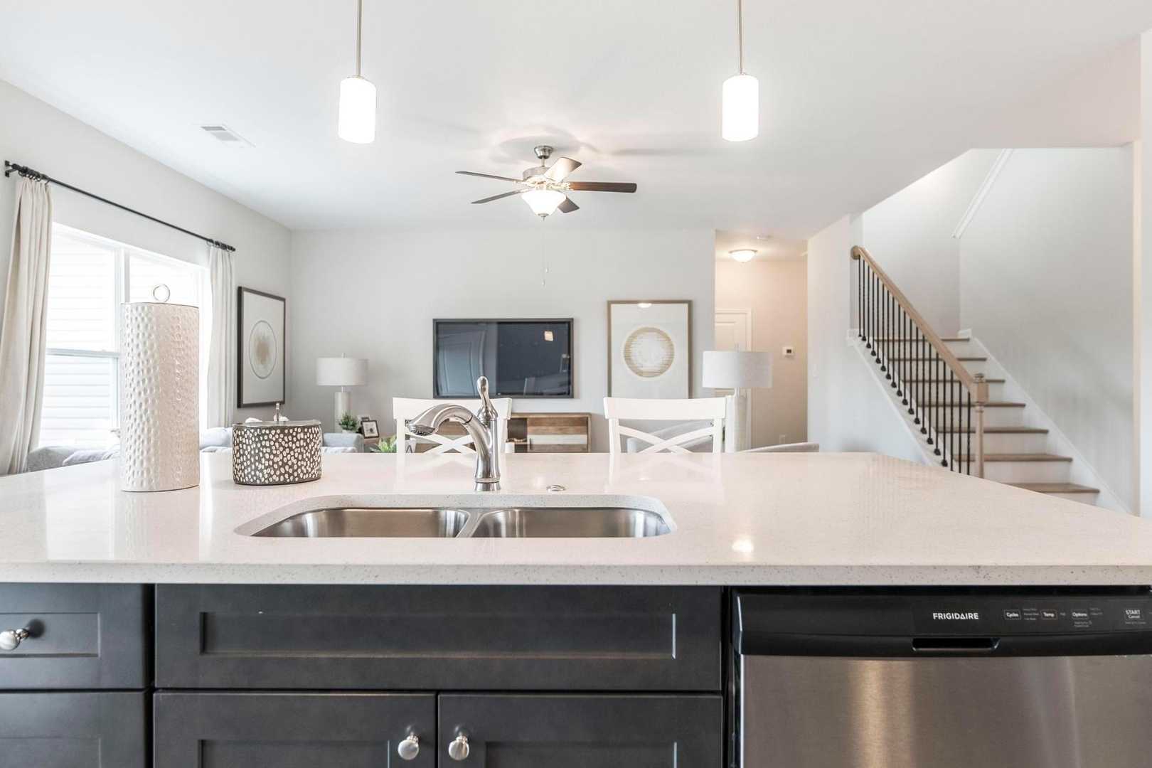 Open-concept kitchen at Cape Reserve Donahue Ridge Auburn AL by Evermore Homes with white quartz island dark cabinets stainless sink and living area view