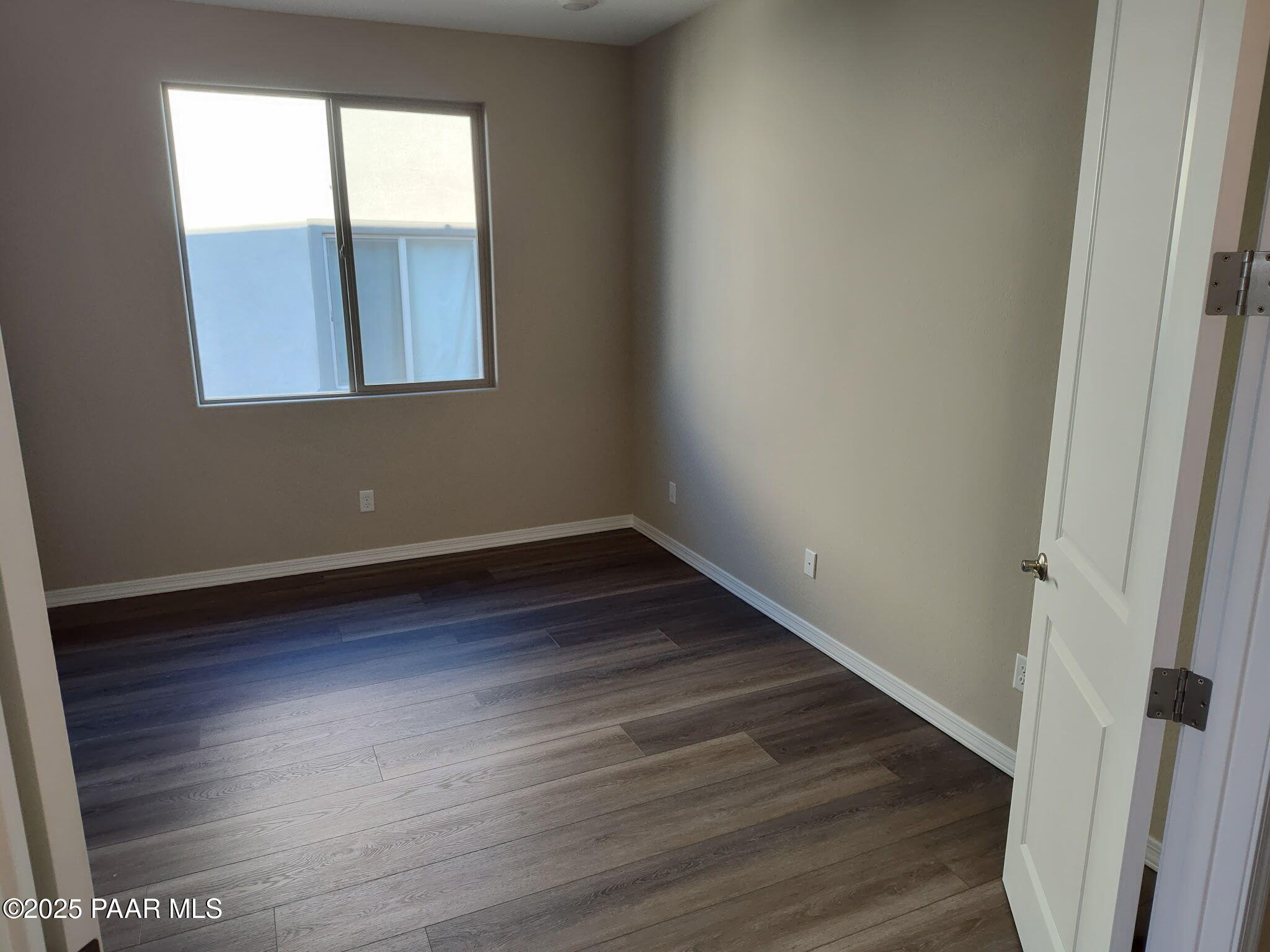 Empty bedroom featuring beige walls, large window with blinds, luxury vinyl plank flooring in Davidson Homes Inspiration A, Prescott Valley AZ