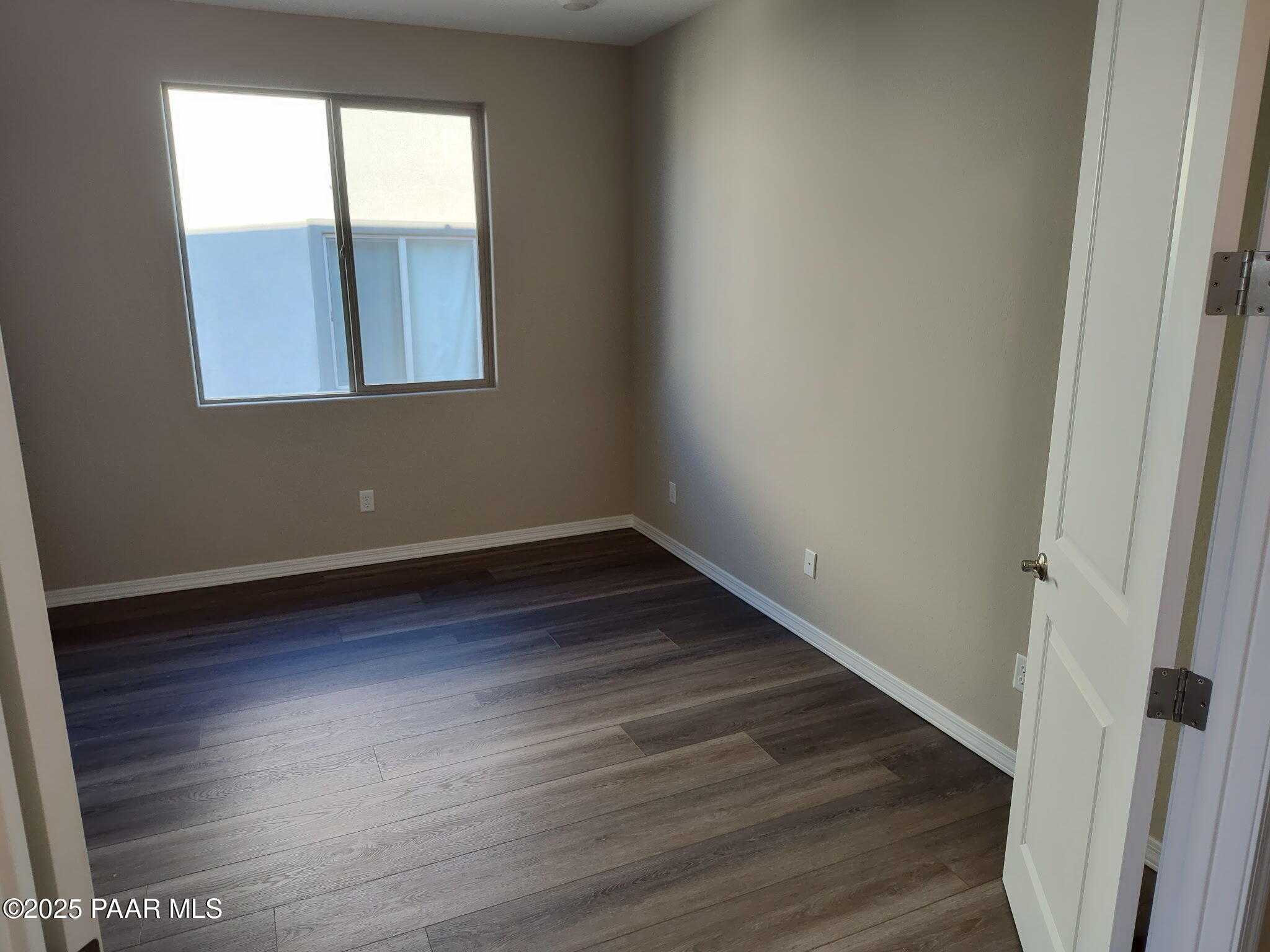 Empty bedroom featuring beige walls, large window with blinds, and luxury vinyl plank flooring in Davidson Homes The Inspiration A, Prescott Valley, Arizona