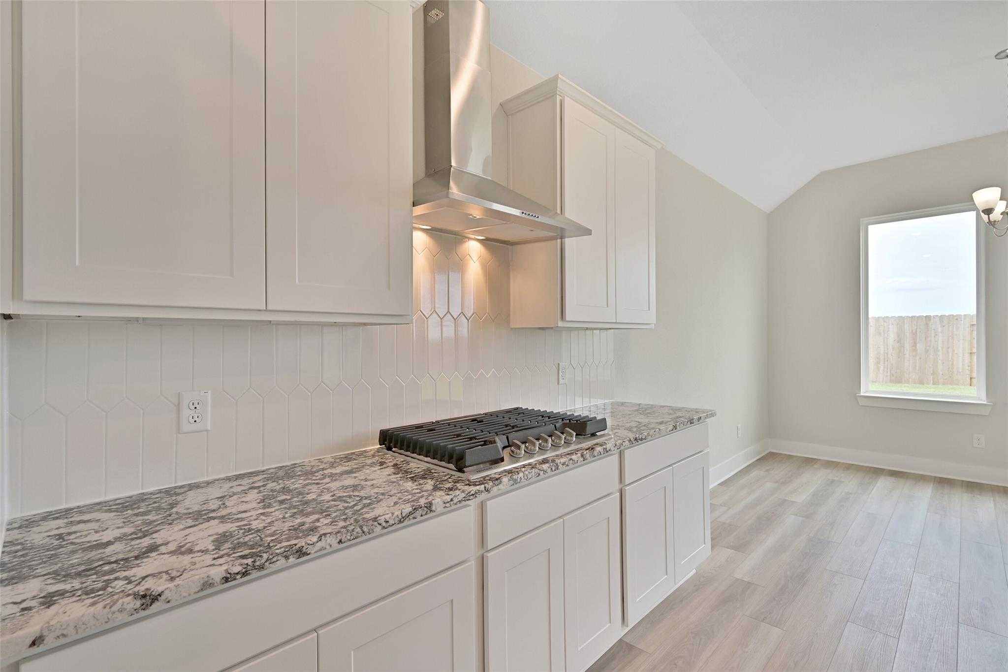 Modern kitchen with white shaker cabinets, speckled quartz counters, gas cooktop, subway tile backsplash in Davidson Homes The Edward A, Lago Mar