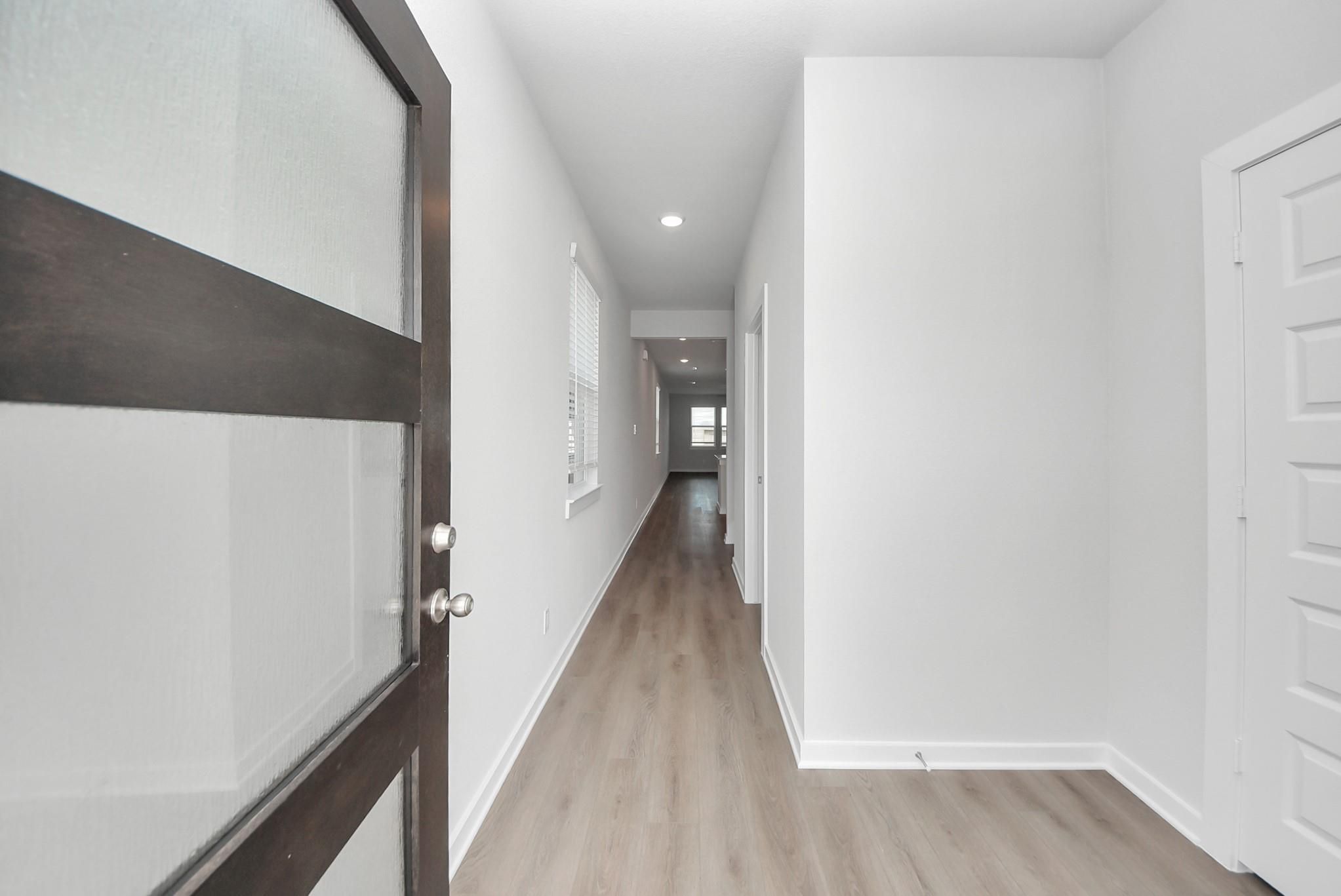 Bright entry hallway with dark wood front door, white walls, and luxury vinyl plank flooring in Davidson Homes The San Marcos E, Beasley, TX