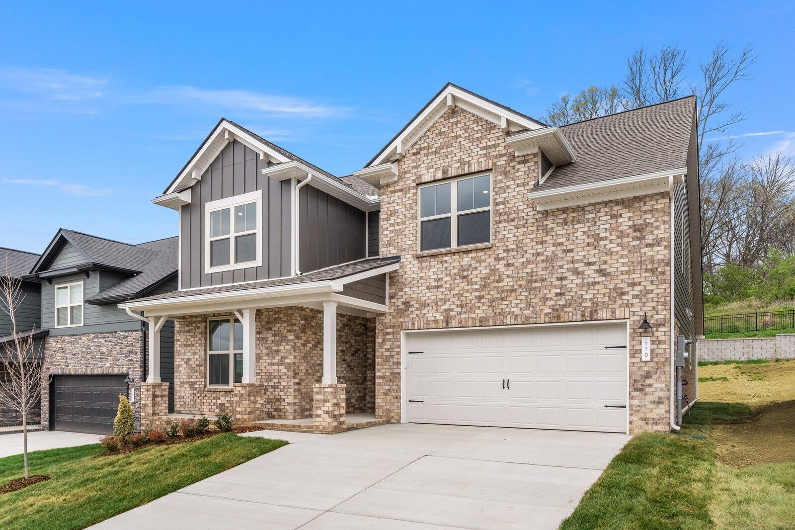 Modern two-story brick home with gray siding, two-car garage, and covered front porch in Woods Crossing, Gallatin, Tennessee