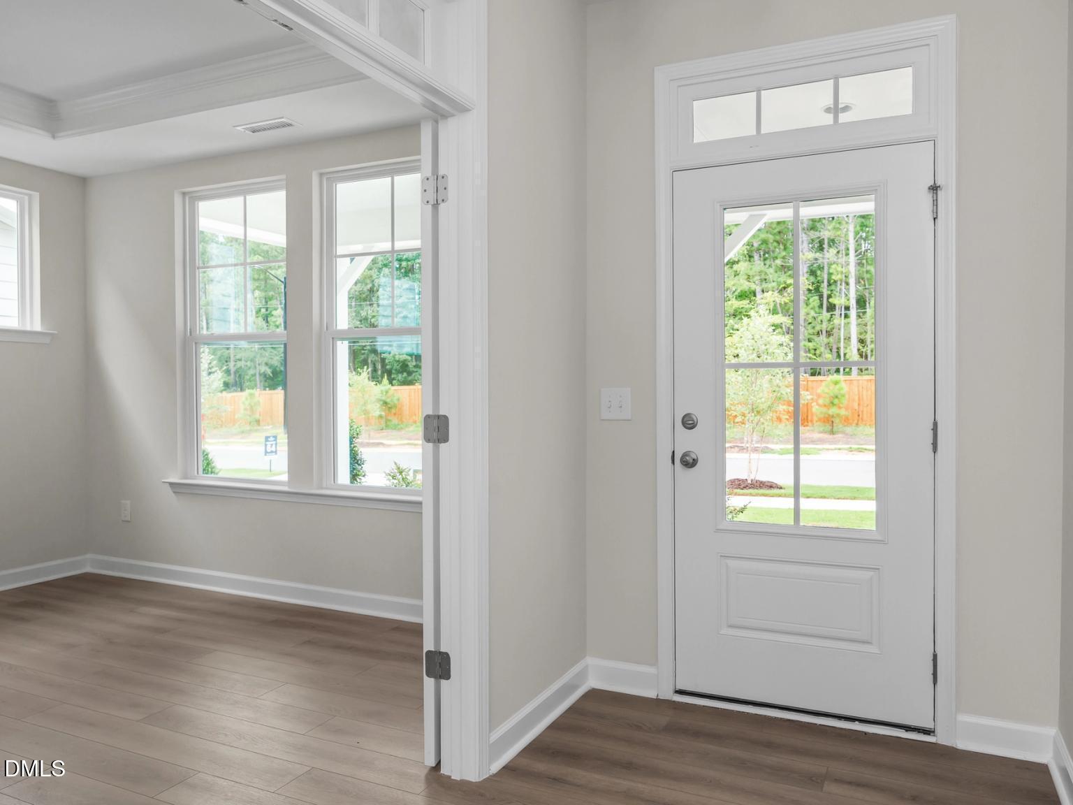 Bright entry foyer with light hardwood floors, large windows, and glass-paneled white door in Davidson Homes The Aspen, Wake Forest