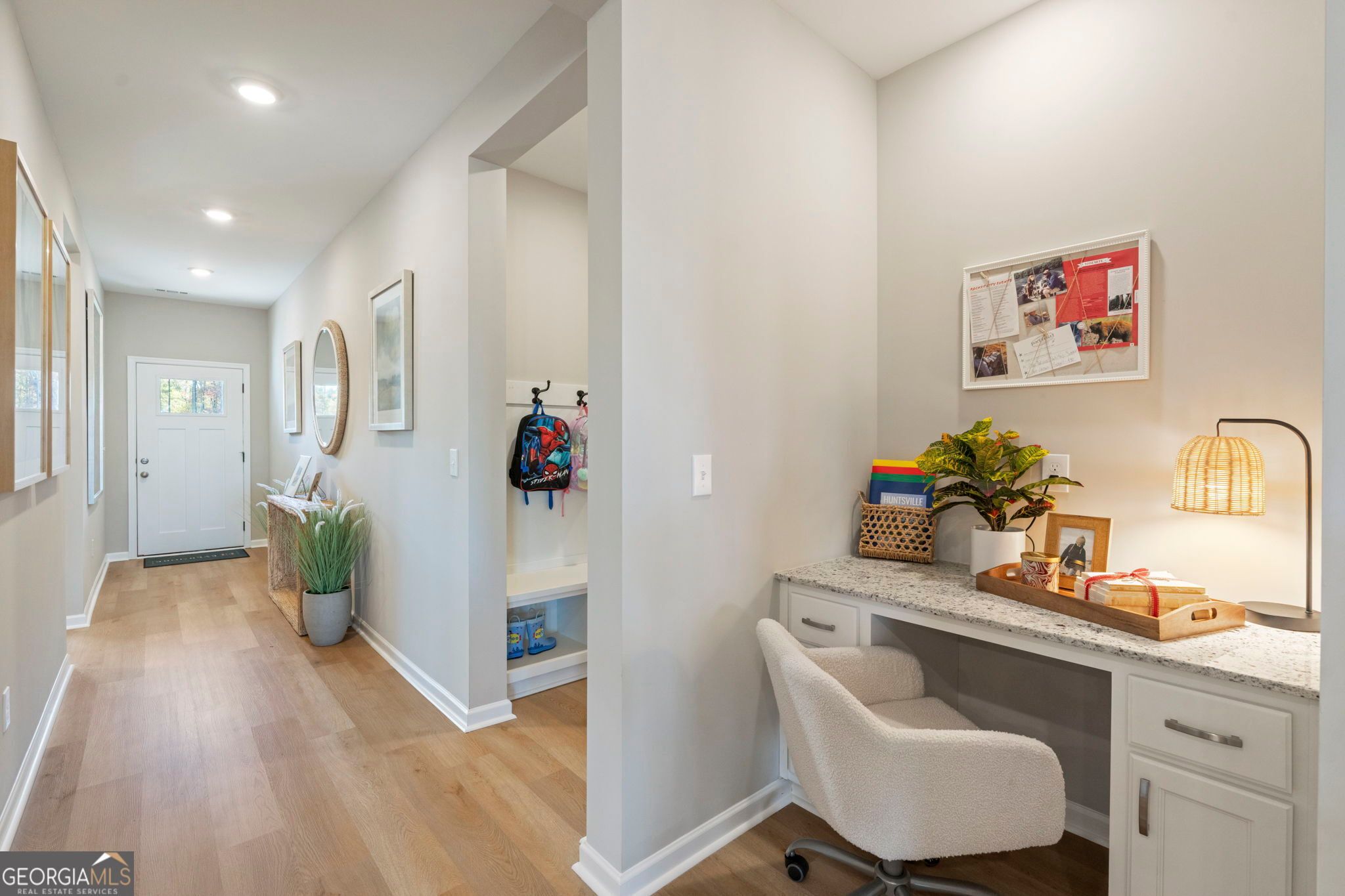 Modern entryway mudroom with built-in bench, backpack hooks, plants, and adjacent home office desk in Evermore Homes The Phoenix, Perry, Georgia