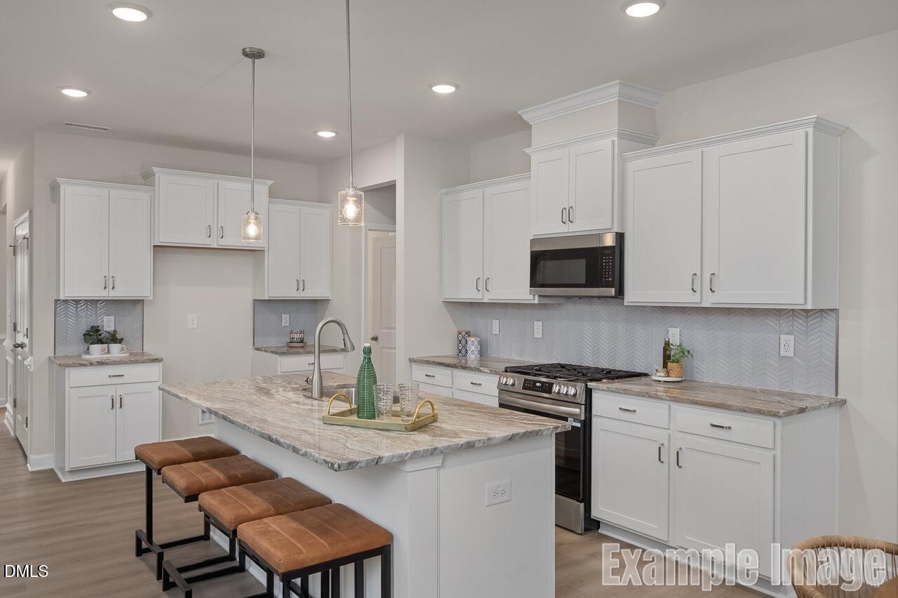 Modern white shaker kitchen with quartz island, stainless steel appliances, and bar stools in The Carter C by Davidson Homes, Lillington NC