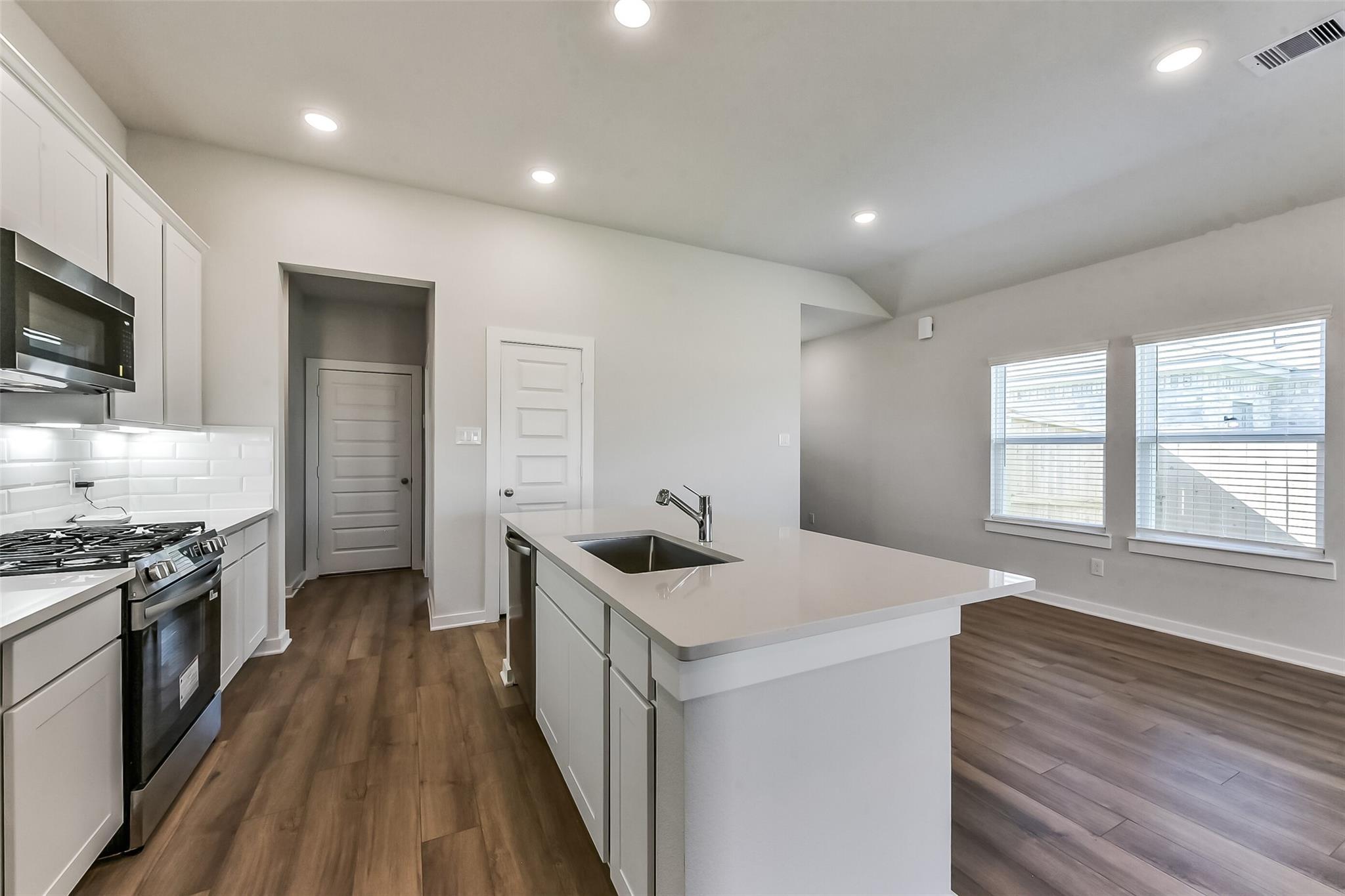 Modern white kitchen with quartz island, stainless appliances, subway tile backsplash in Davidson Homes Costa C, Dayton TX