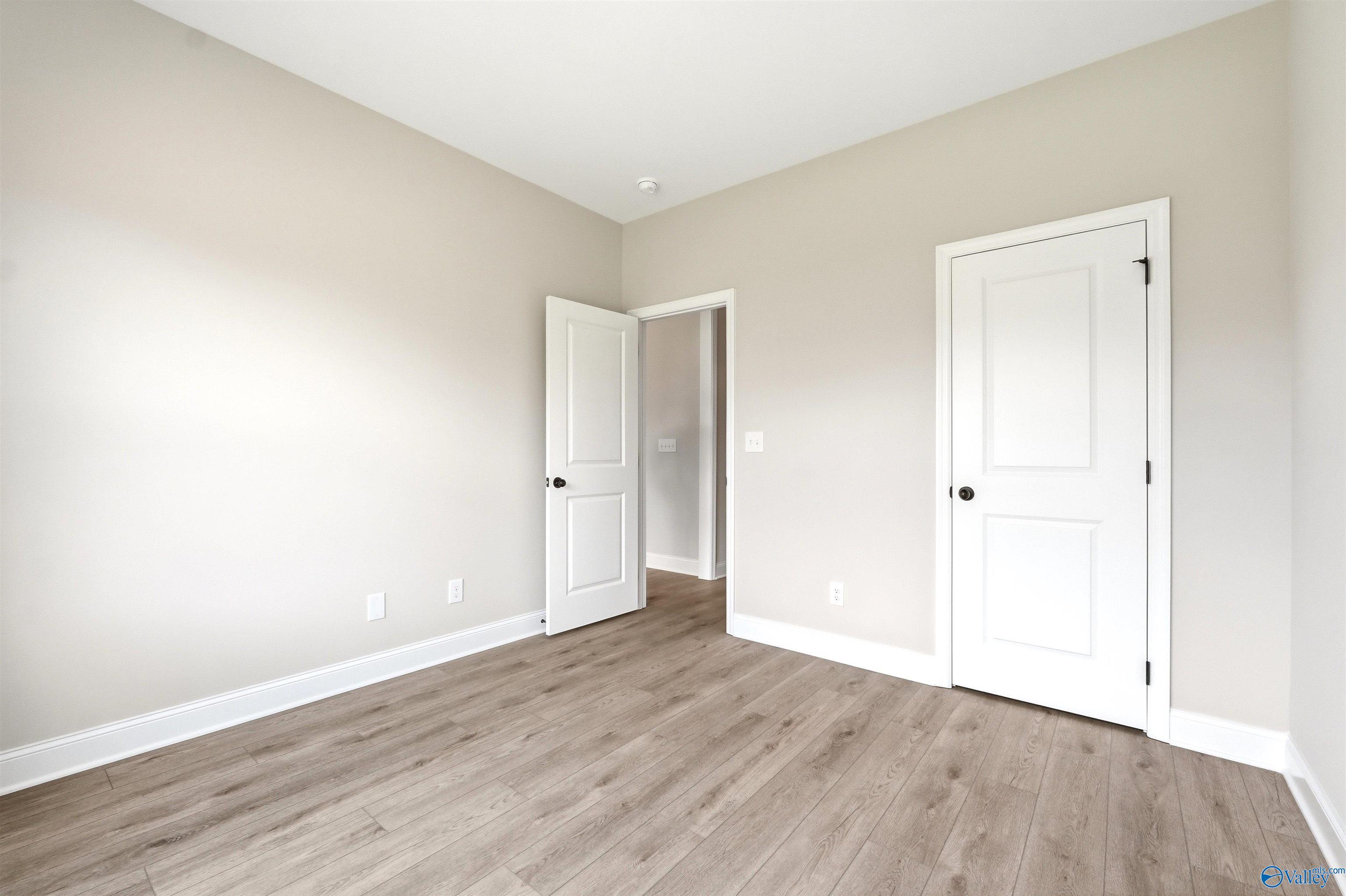 Spacious bedroom with neutral paint and hardwood-style flooring in The Shelby A floor plan at Wood Trail, Toney, Alabama.