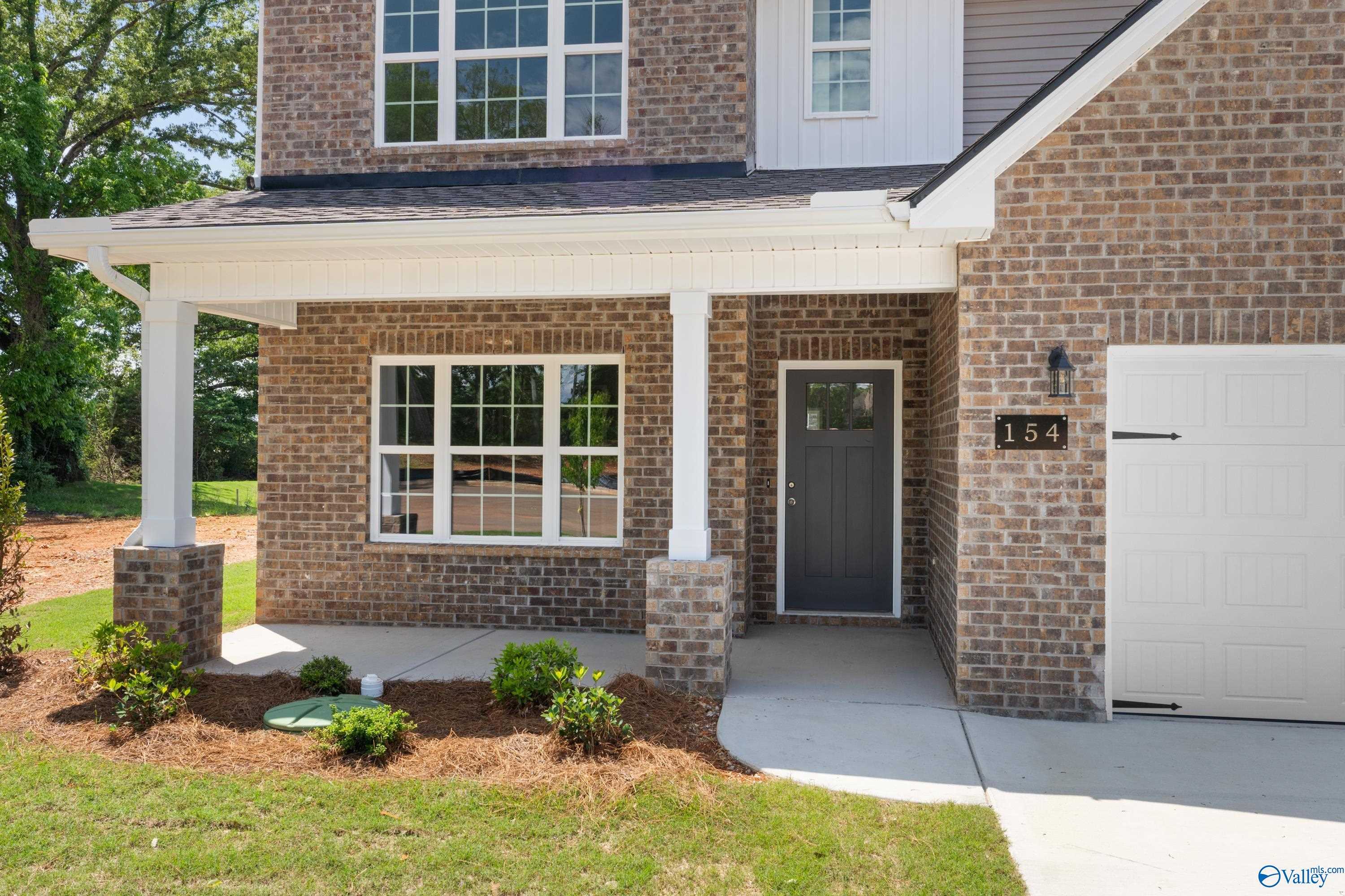 Two-story brick home with covered front porch, white columns, large windows, and two-car garage in Creek Grove, New Market, Alabama