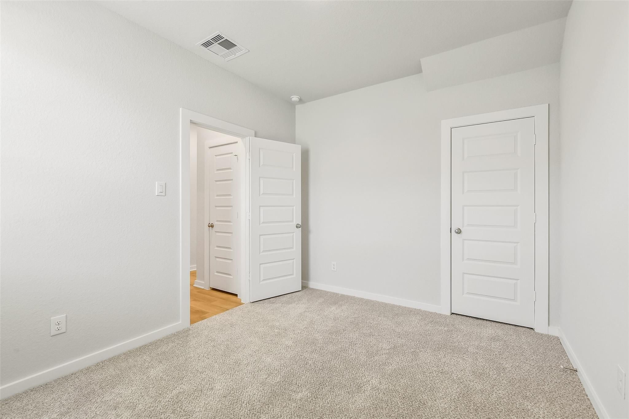 Bright secondary bedroom featuring white paneled doors, beige carpet, and open adjoining space in 5-bedroom San Marcos E home, Cleveland, Texas