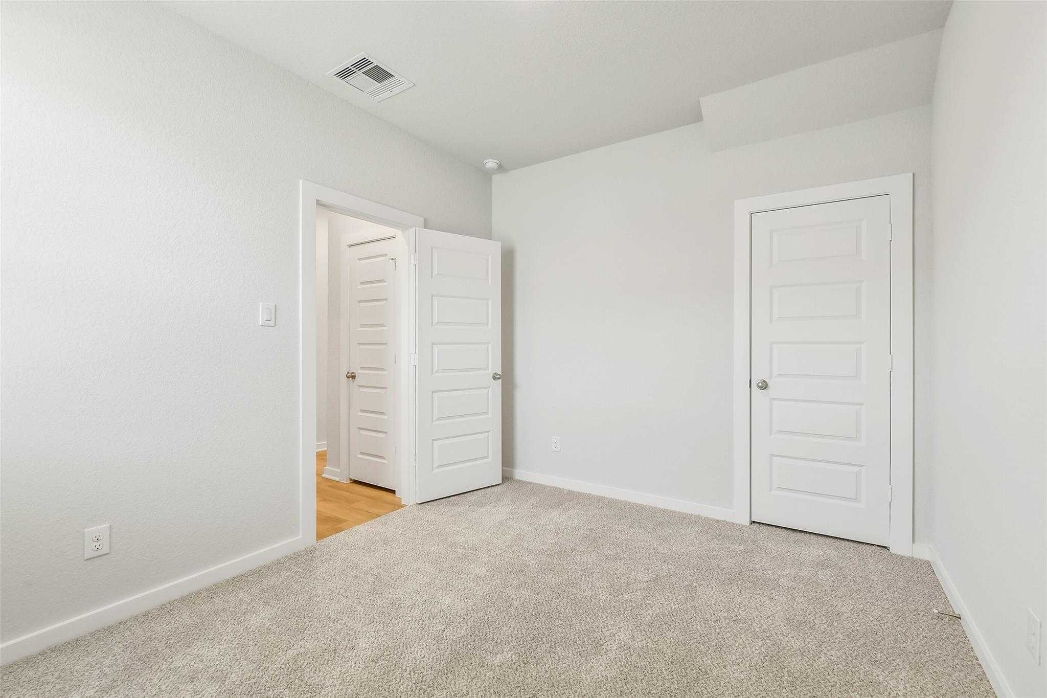 Bright secondary bedroom featuring white paneled doors, beige carpet, and open adjoining space in 5-bedroom San Marcos E home, Cleveland, Texas