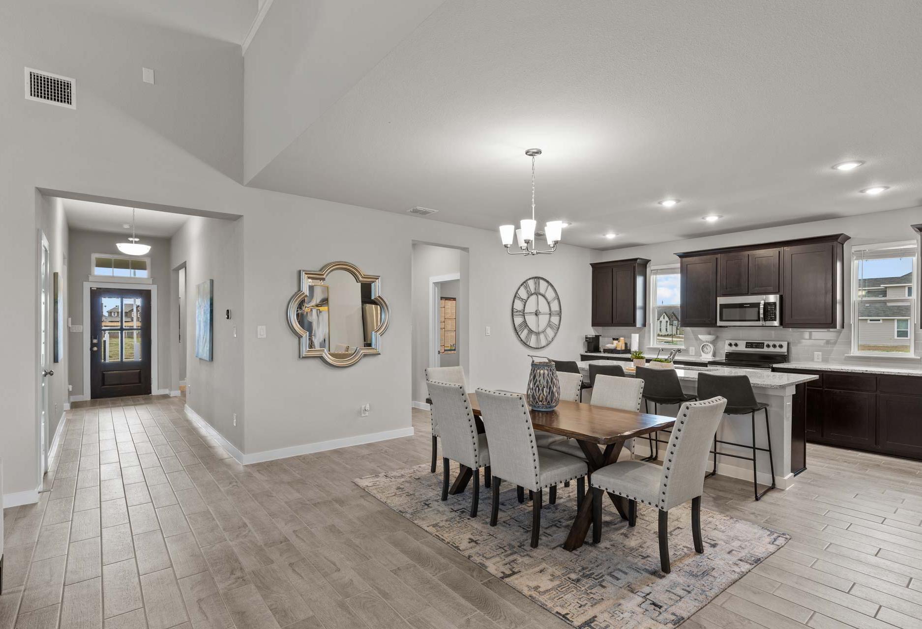 Open-concept dining and kitchen in The Collin A home, featuring dark wood cabinets, large island, upholstered chairs, and entry hallway