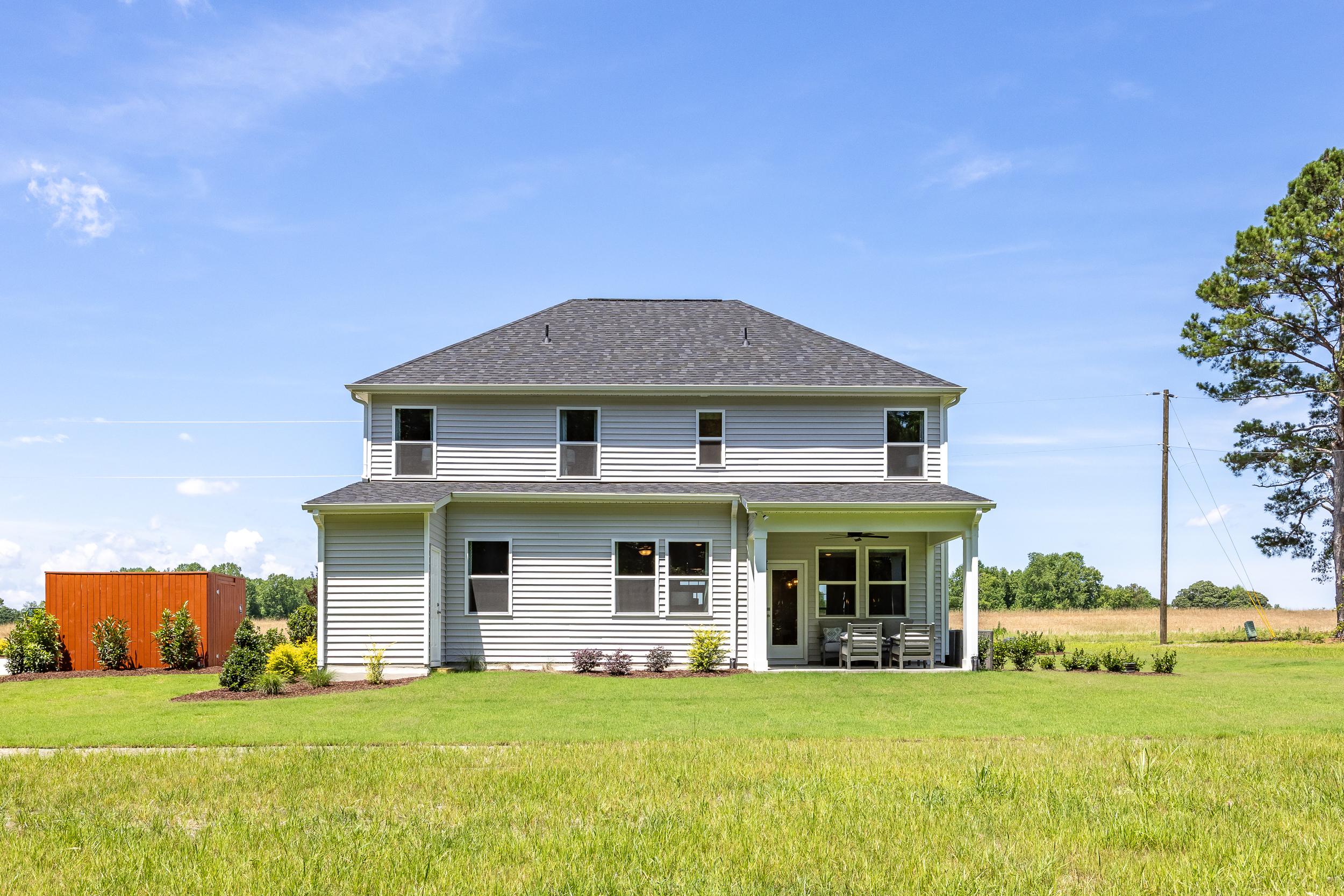 Two-story gray farmhouse exterior at Retreat at North Main in Lillington NC with covered porch, green lawn, and pine trees