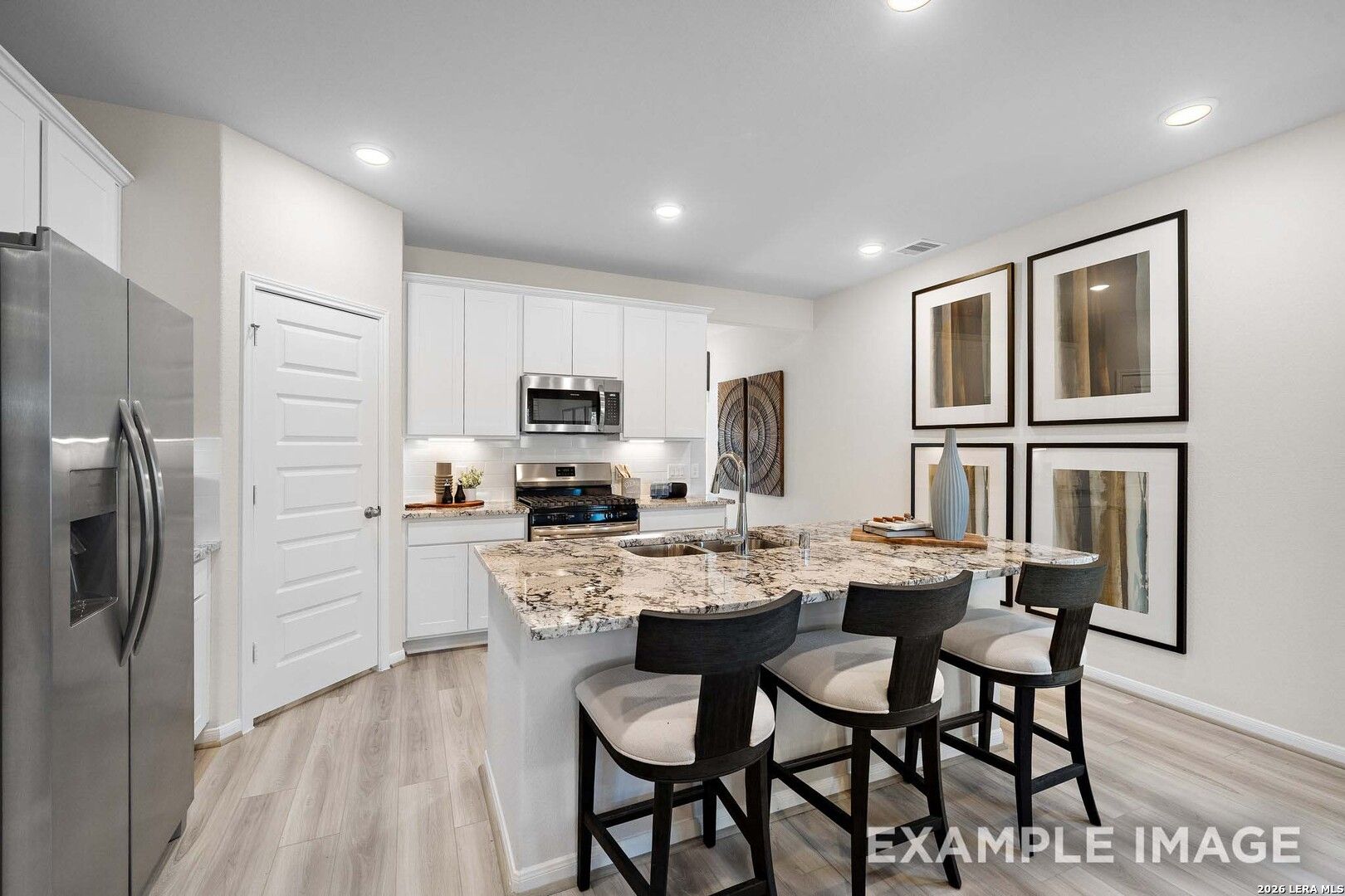 Modern kitchen with granite island, white cabinets, and stainless appliances in The San Marcos F, Rayburn Valley, San Antonio.