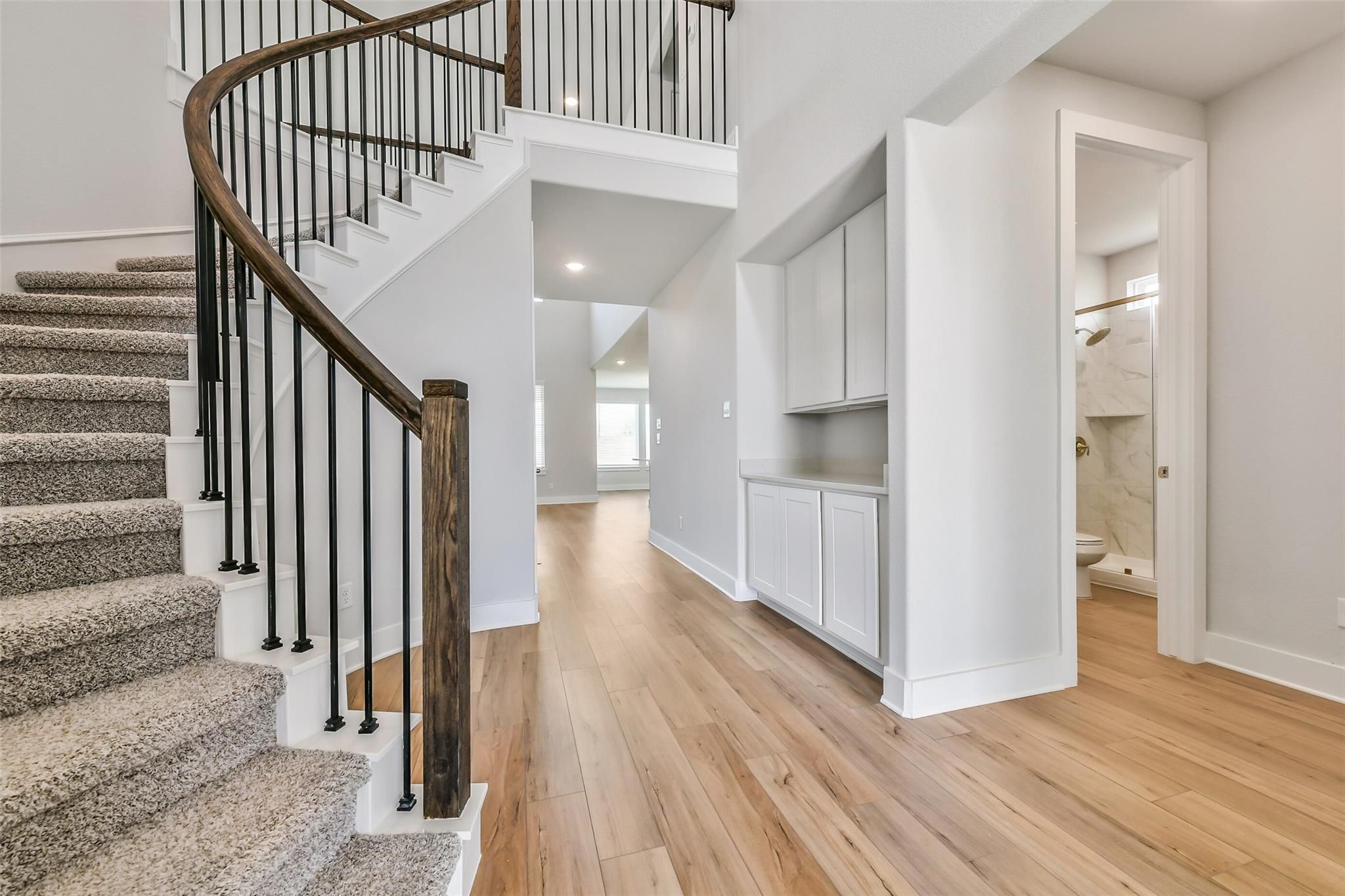 Elegant curved wooden staircase with black railings in two-story foyer, hardwood floors, built-in cabinet, and marble bathroom in Davidson Homes The Victoria A, Lago Mar, Texas City