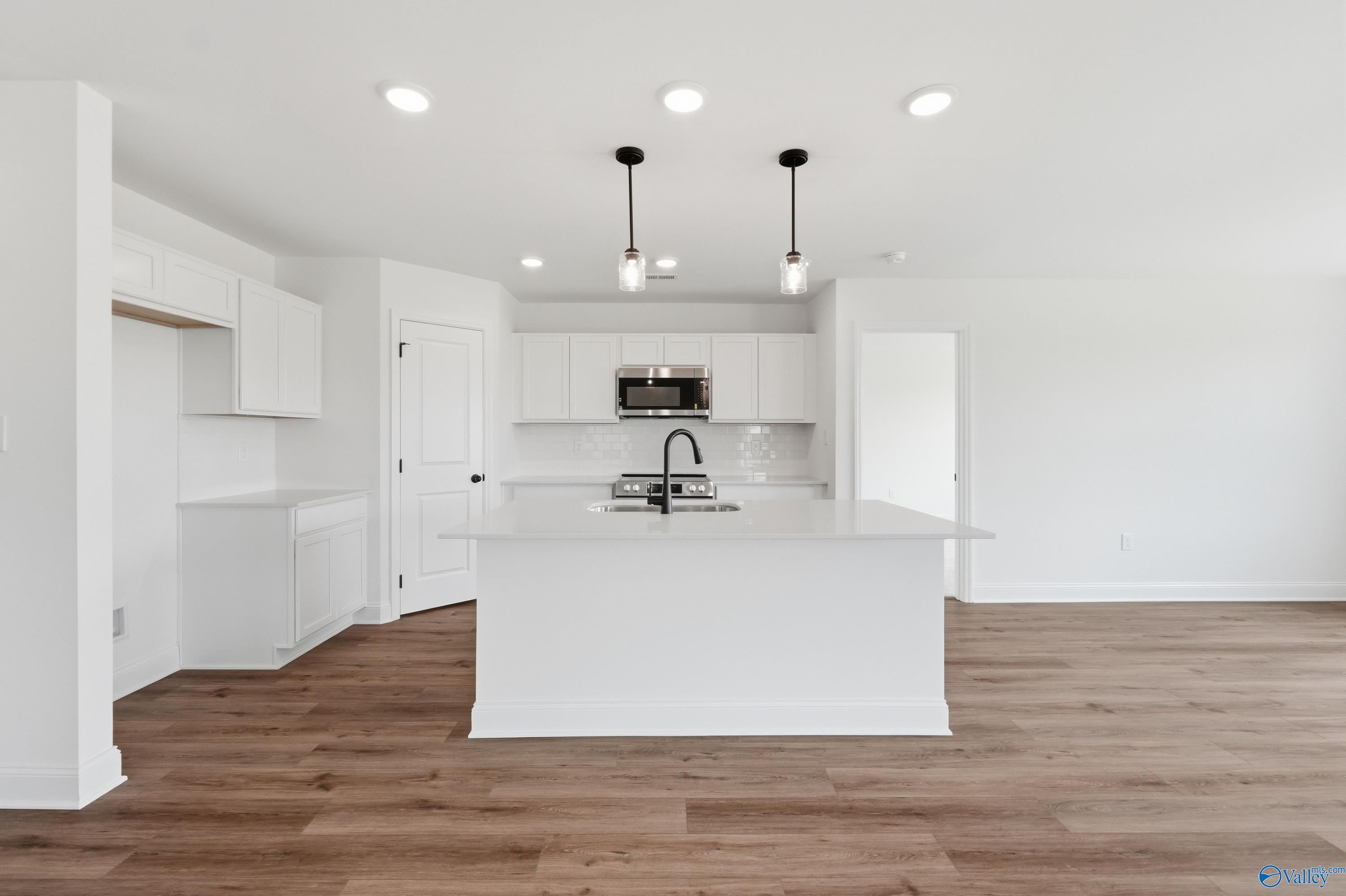 Modern kitchen with white cabinets, center island, and wood-style flooring in The Franklin floor plan, New Market, AL.