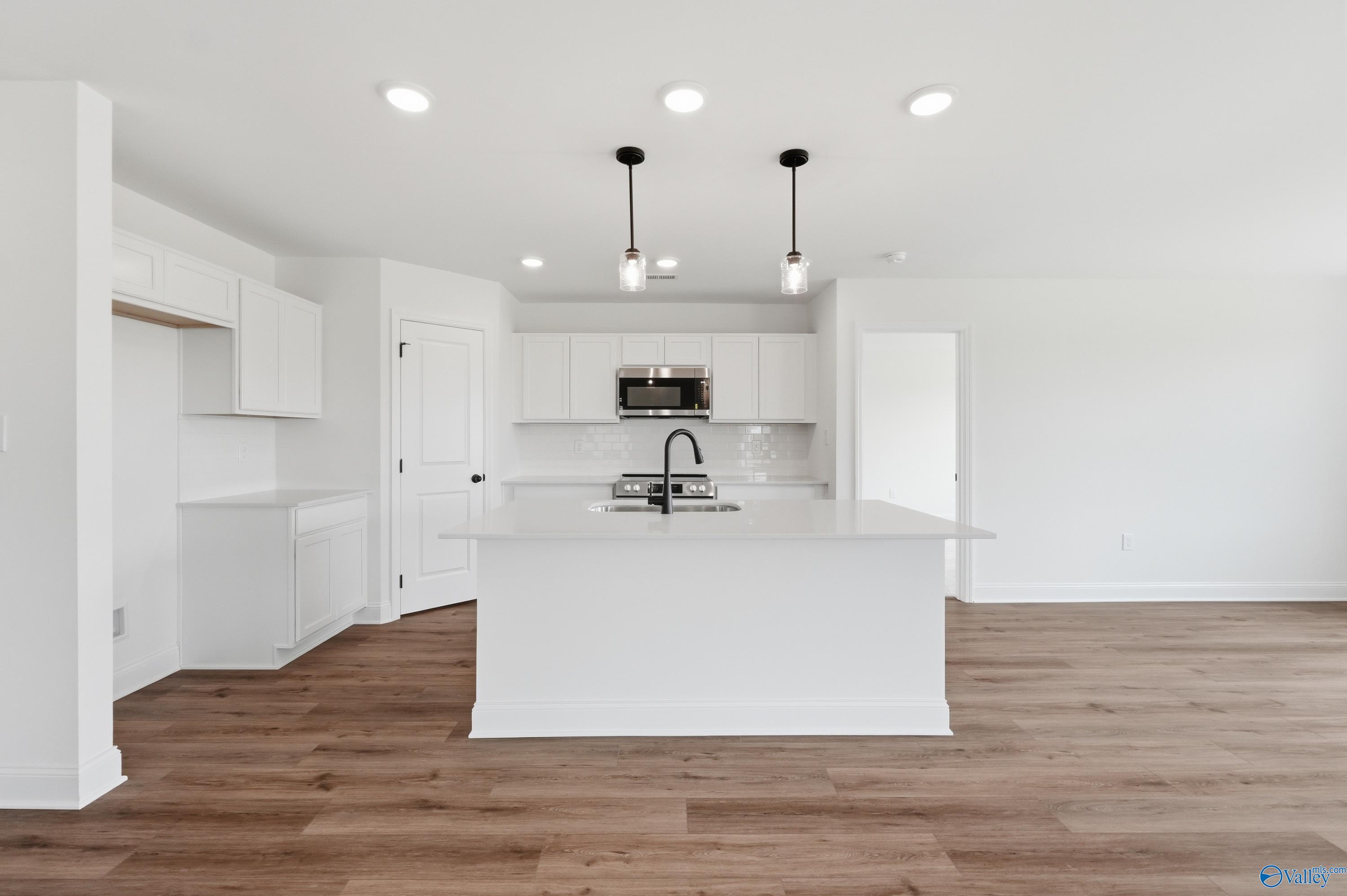 Modern kitchen with white cabinets, center island, and wood-style flooring in The Franklin floor plan, New Market, AL.