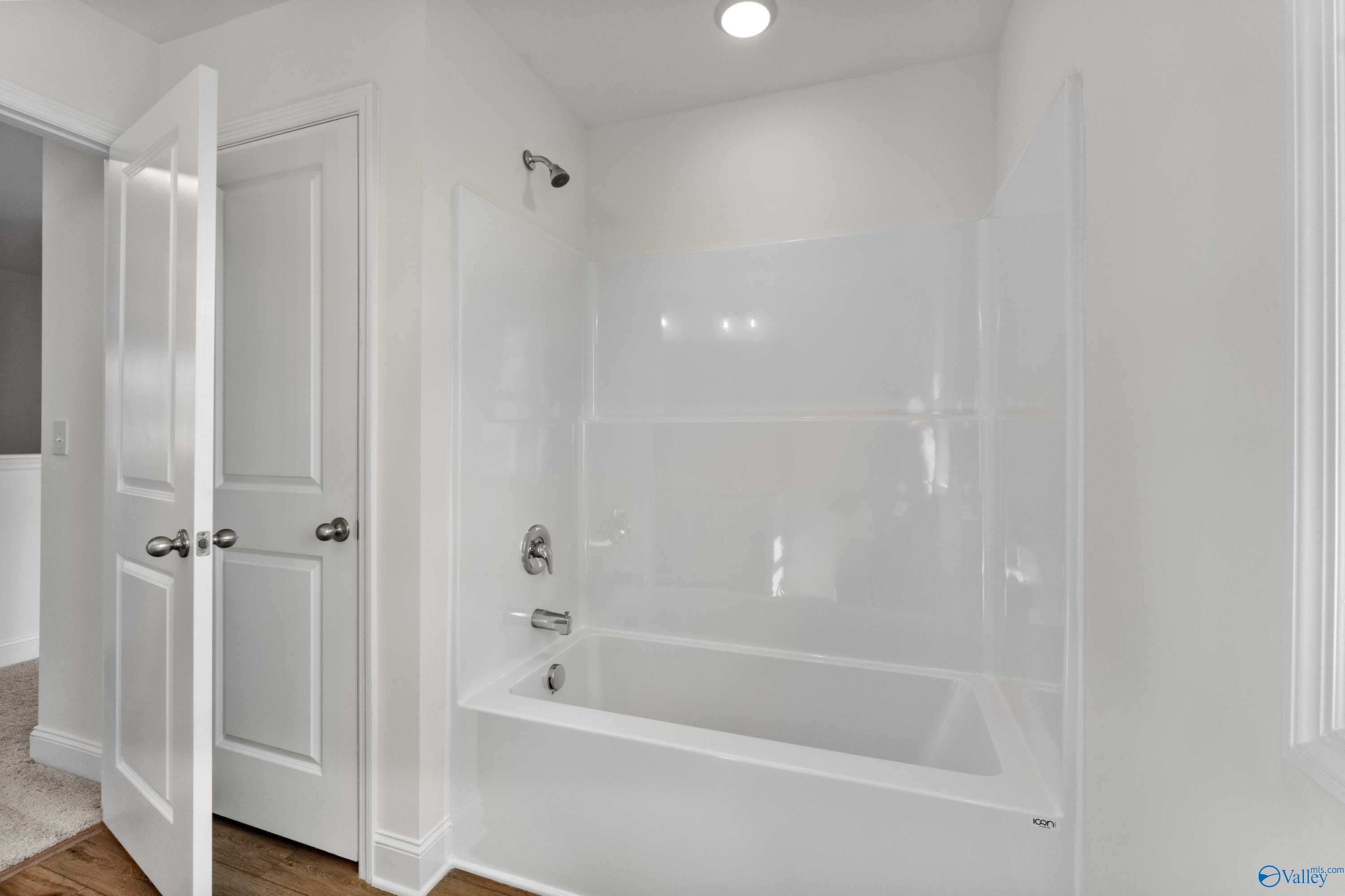 Bright white bathroom with bathtub, shower combo, and tiled walls in Davidson Homes The Shelby A, New Market, Alabama